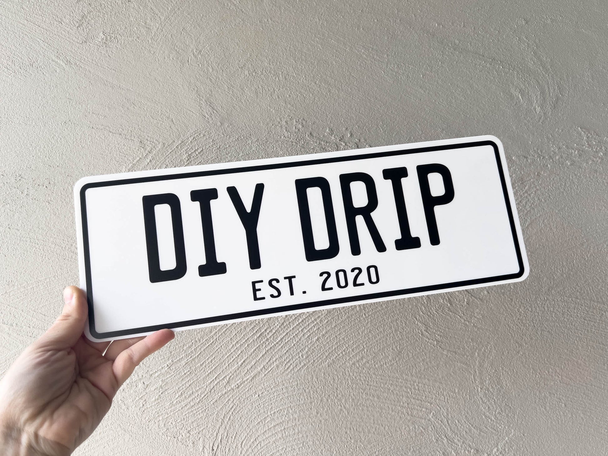 Hand holding an acrylic plate with 'DIY DRIP EST. 2020' text against a plain background