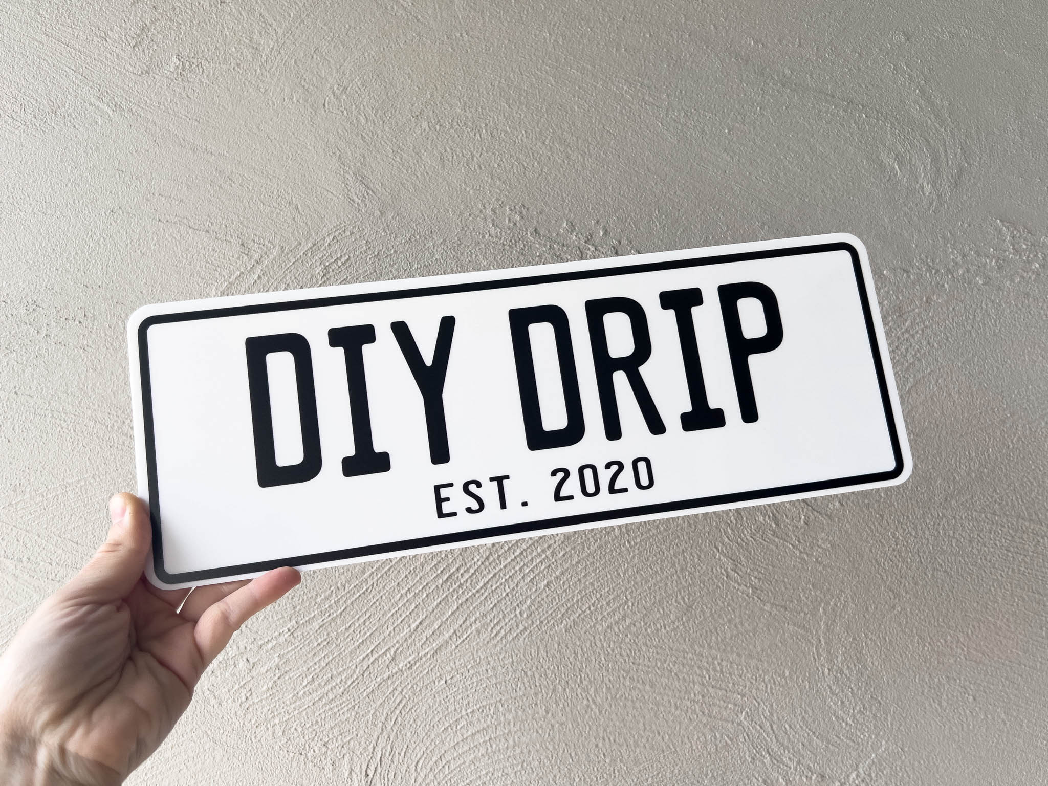 Hand holding an acrylic plate with 'DIY DRIP EST. 2020' text against a plain background
