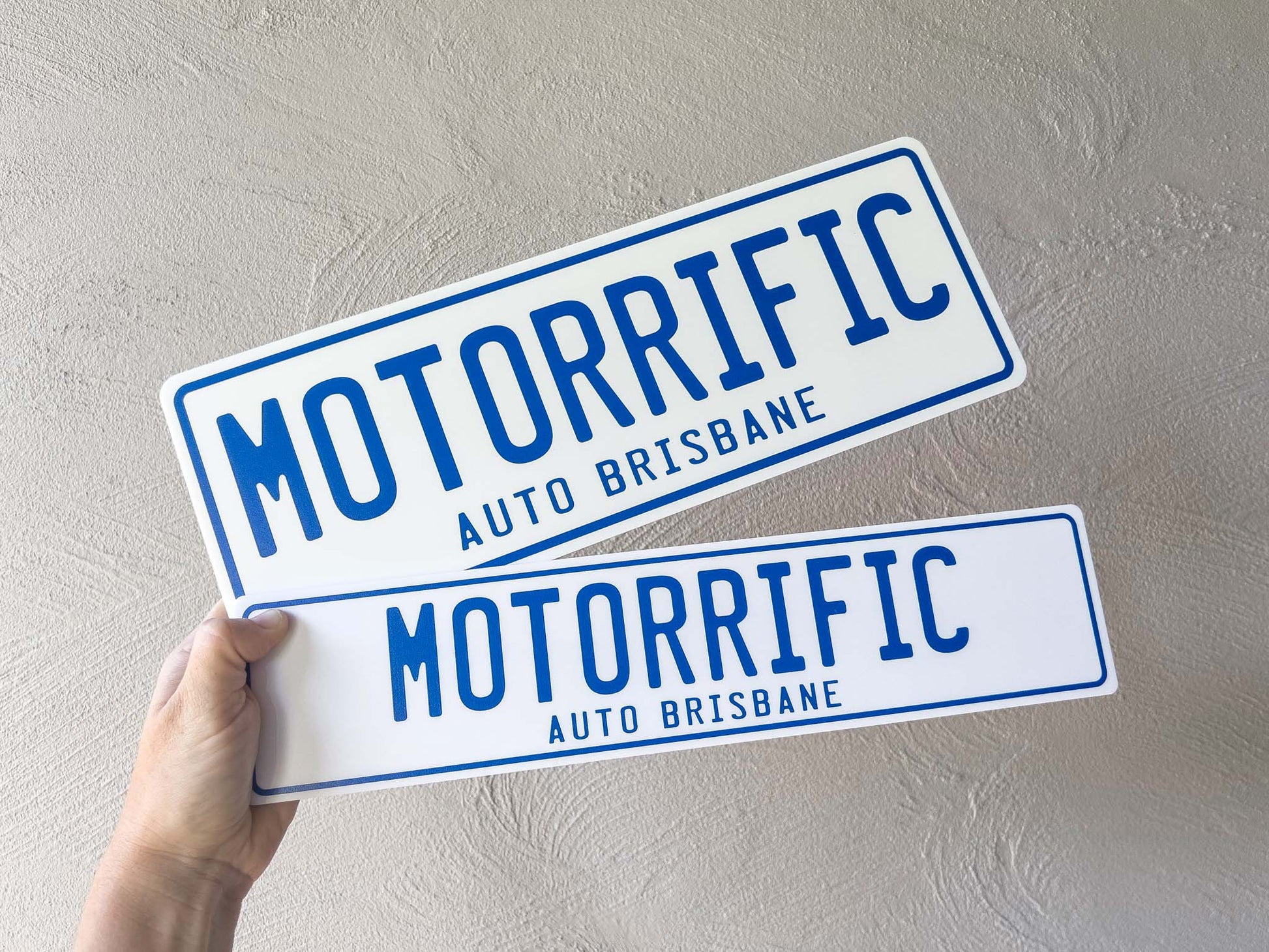 Two 'Motorrific Auto Brisbane' acrylic plates held against a light grey background