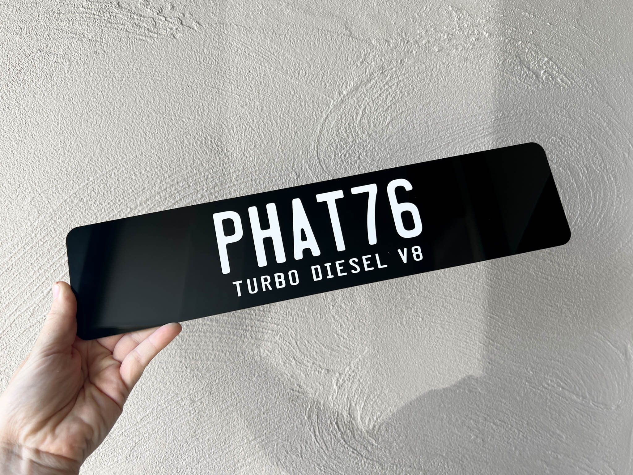 Black slim style acrylic cover plate with 'PHAT76 TURBO DIESEL V8' text held against a light grey background