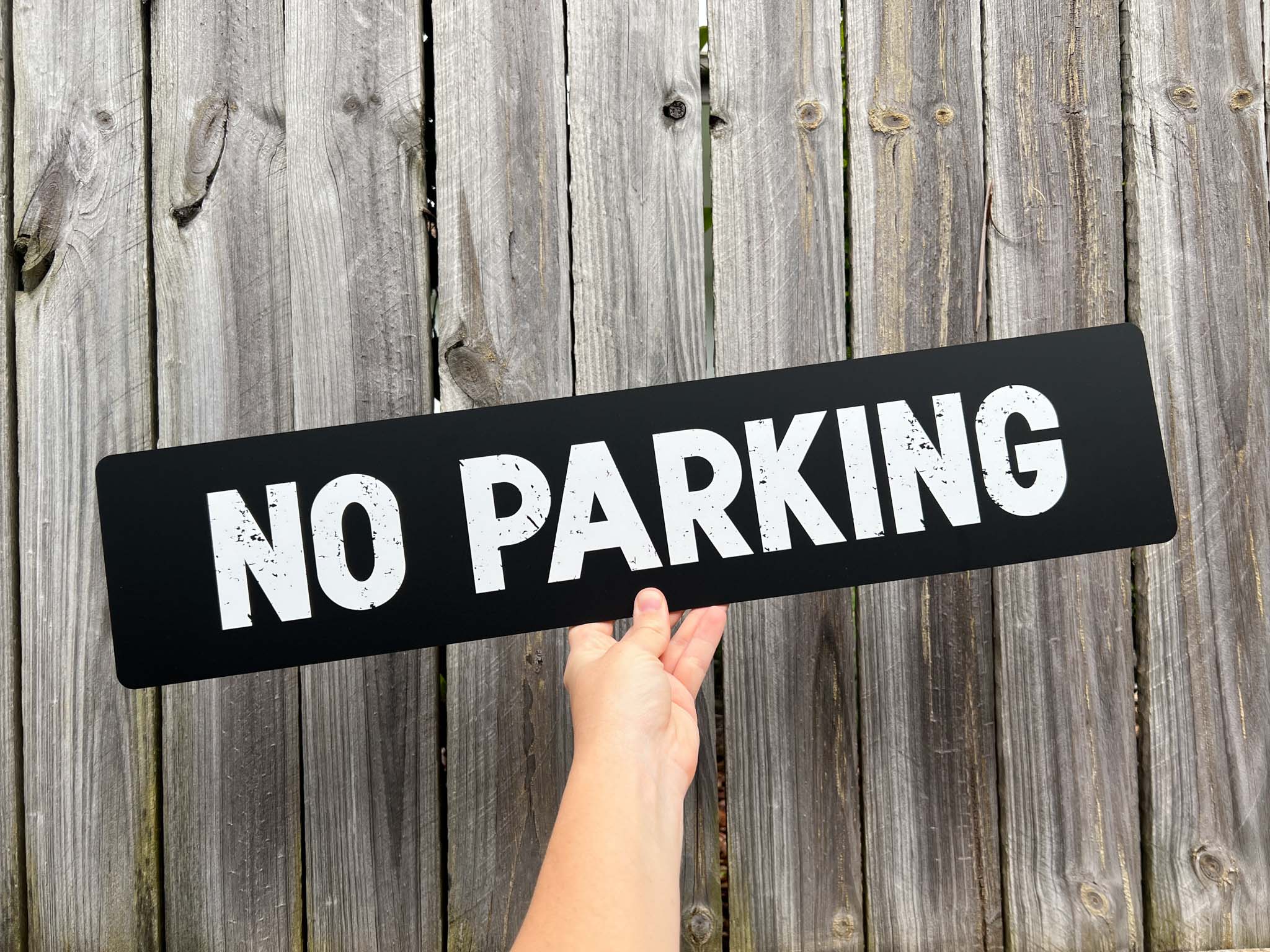 A weathered textured print custom text sign that says 'NO PARKING'.