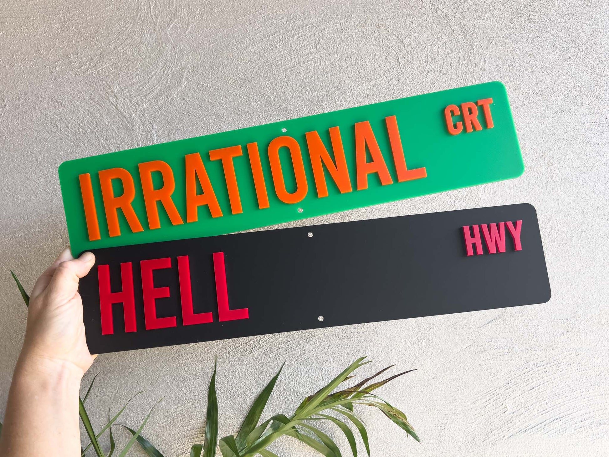 Two novelty street signs with humorous text held by a hand against a light background.