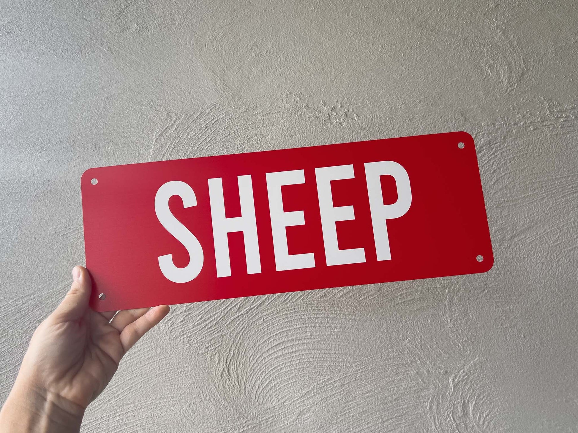 A personalised red metal cover plate with the word 'SHEEP' printed in white text.
