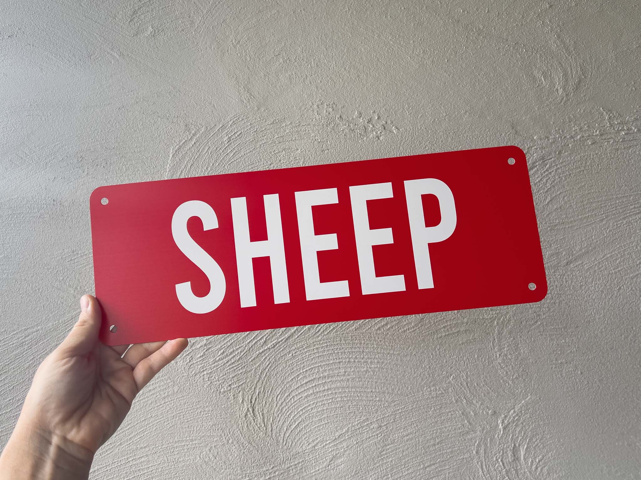A personalised red metal cover plate with the word 'SHEEP' printed in white text.