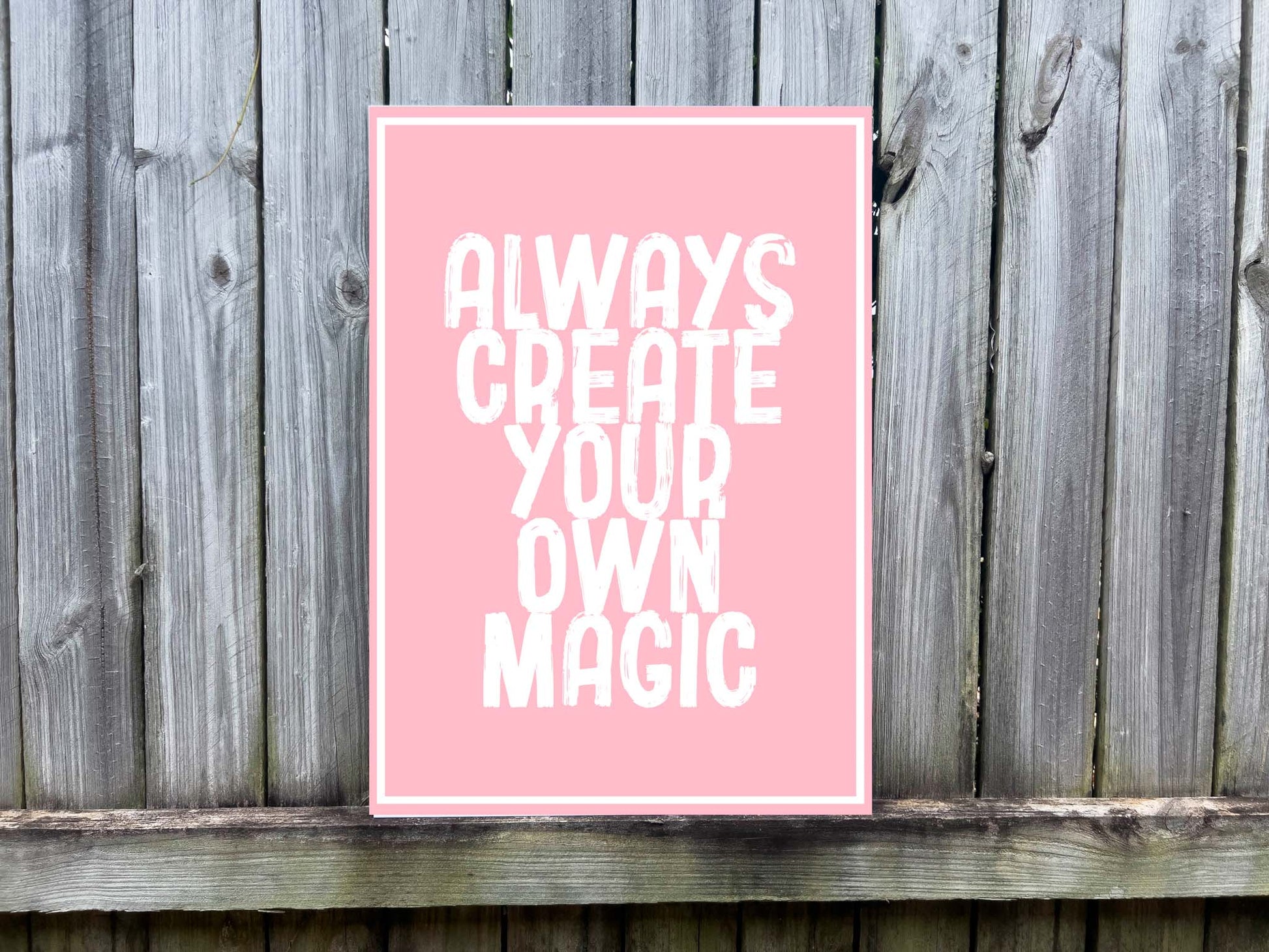 Pink UV printed sign with 'Always Create Your Own Magic' white text on a wooden background
