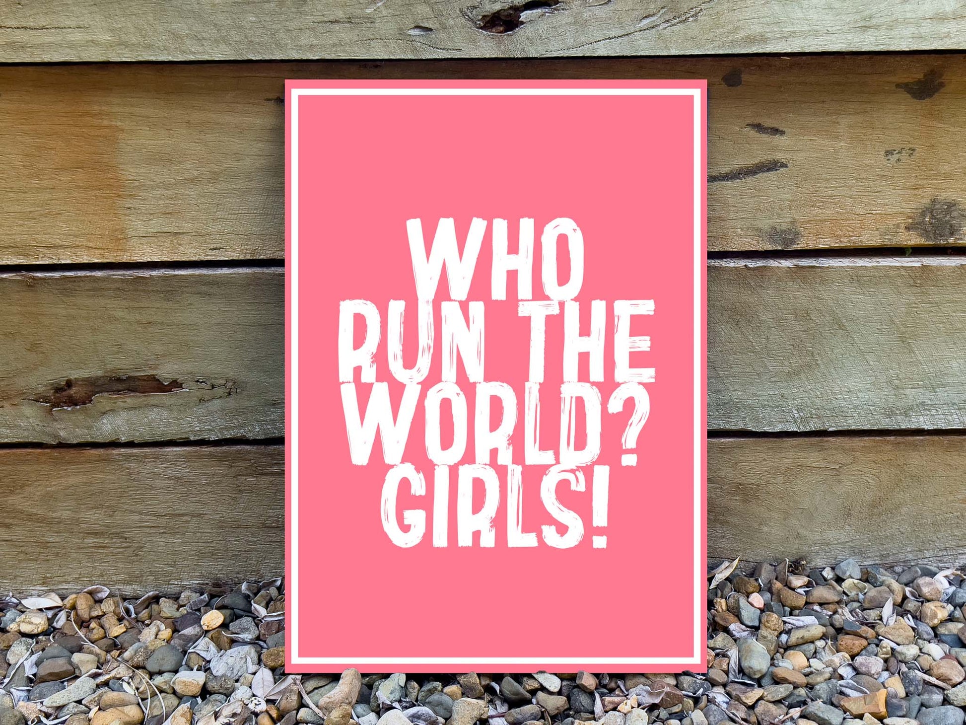 Pink sign with 'WHO RUN THE WORLD? GIRLS!' text on a wooden background