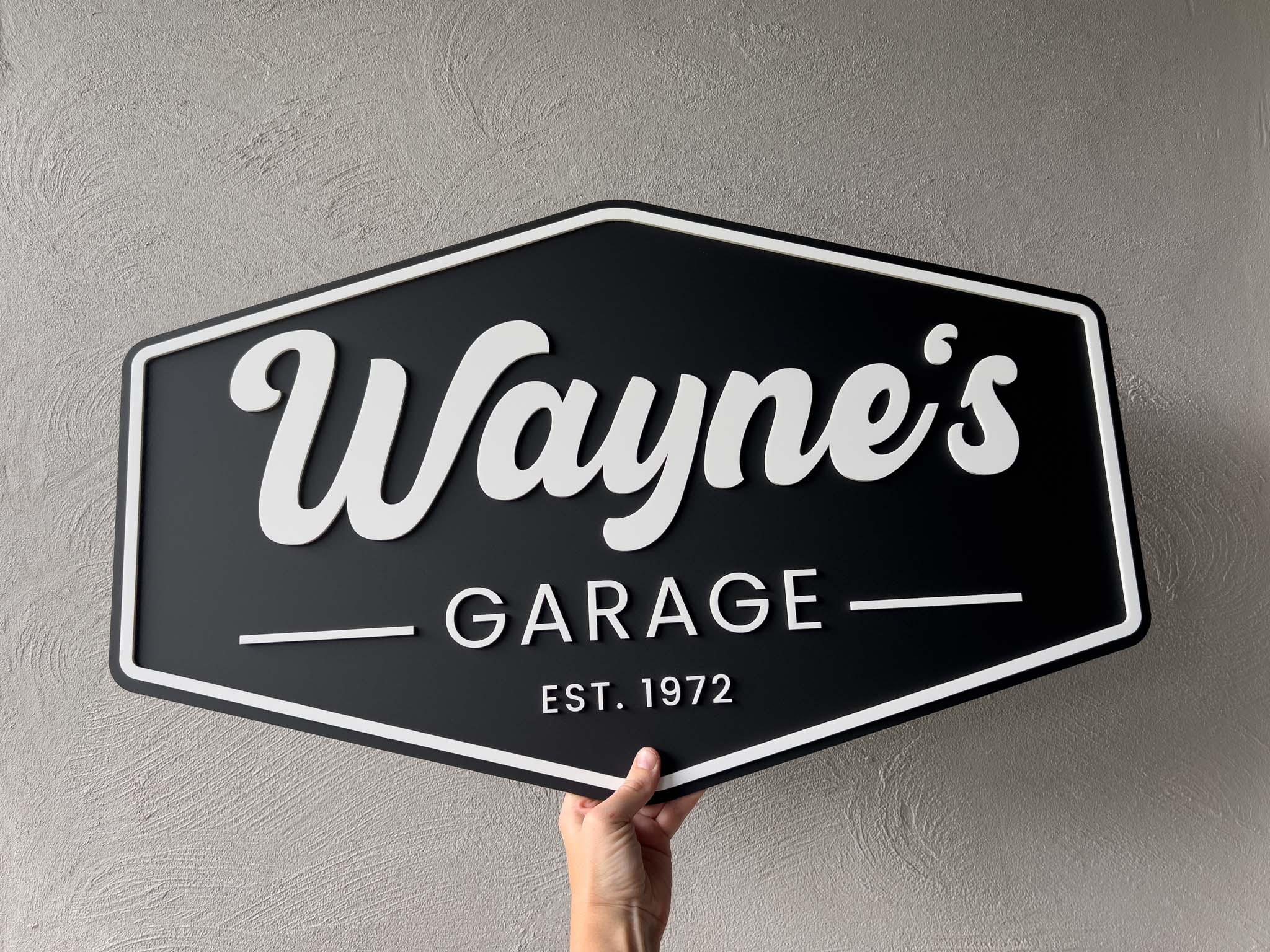 A custom black and white sign made in 3D acyrylic layers that reads 'Wayne's Garage Est. 1972'.