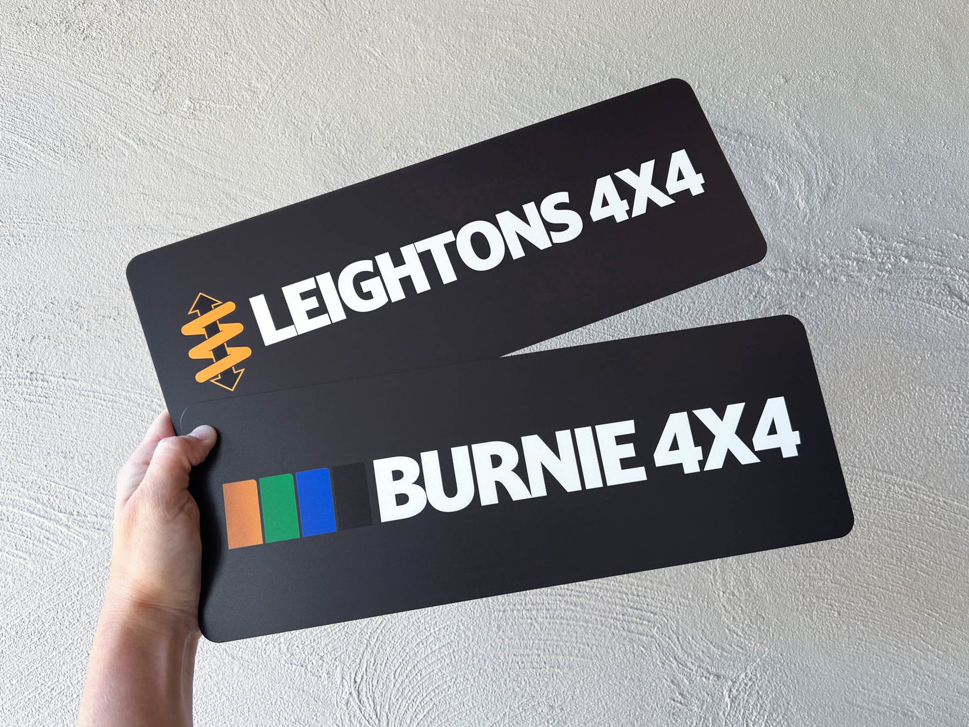 Two black license plates with 'Leightons 4X4' and 'Burnie 4X4' branding held by a hand against a light grey background.