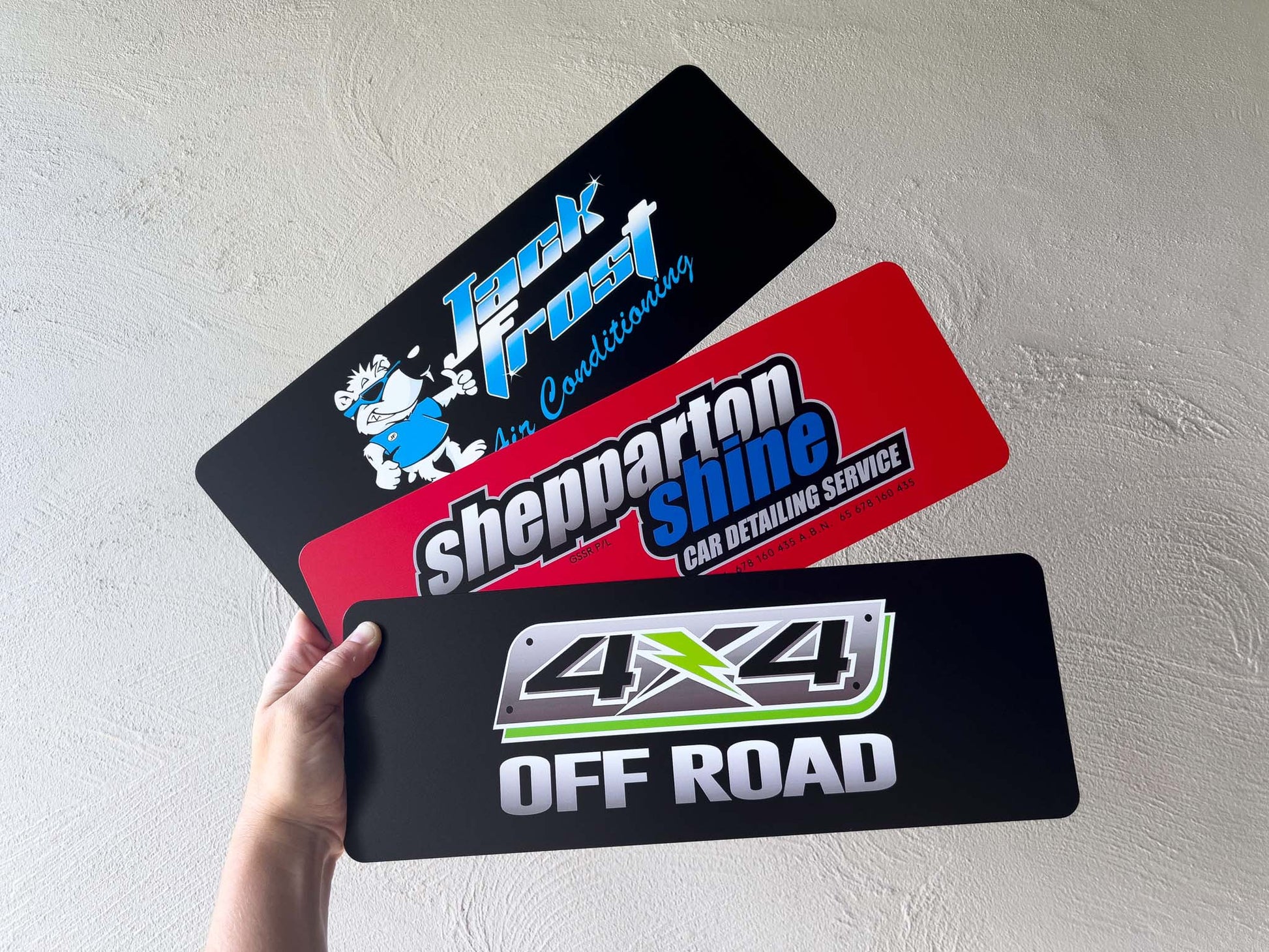 Collection of logo plates with different branding held by a hand against a light grey background.