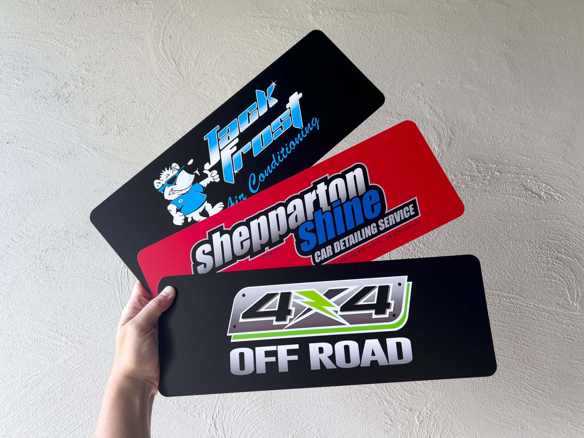 Collection of logo plates with different branding held by a hand against a light grey background.