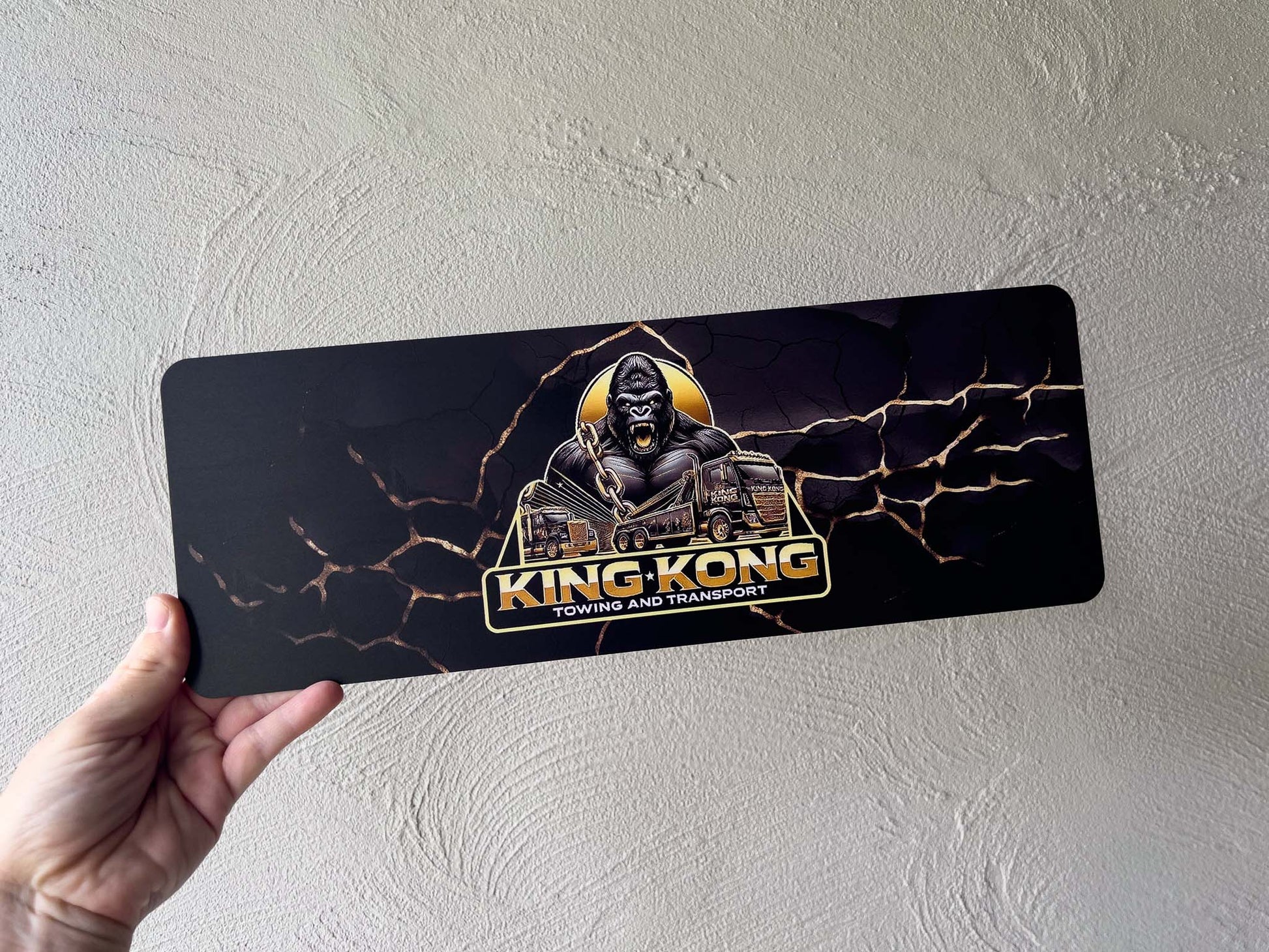 Hand holding a King Kong towing and transport logo plate sign against a plain background