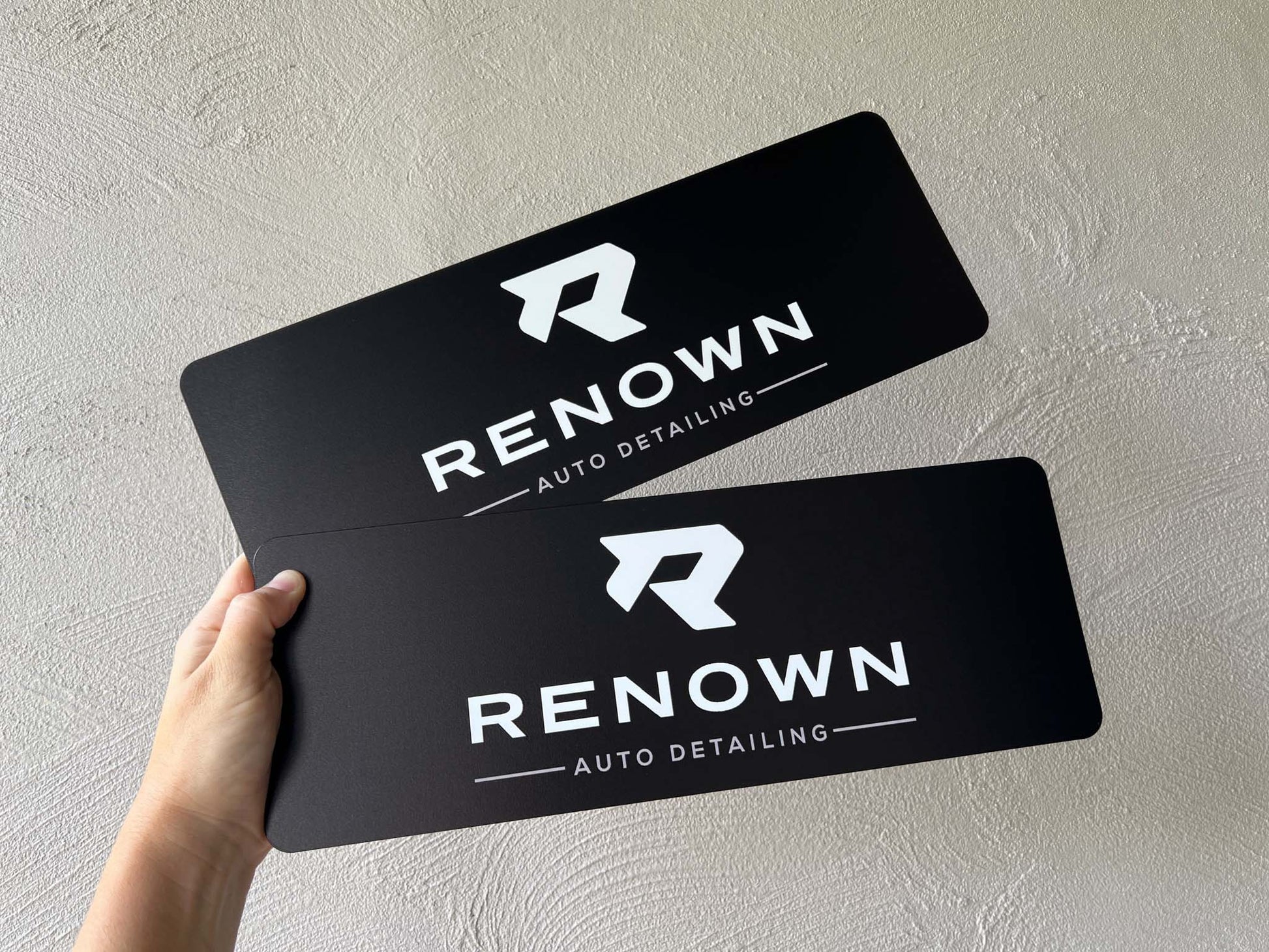 Two black and white UV printed logo paltes with 'Renown Auto Detailing' logo held against a light grey background