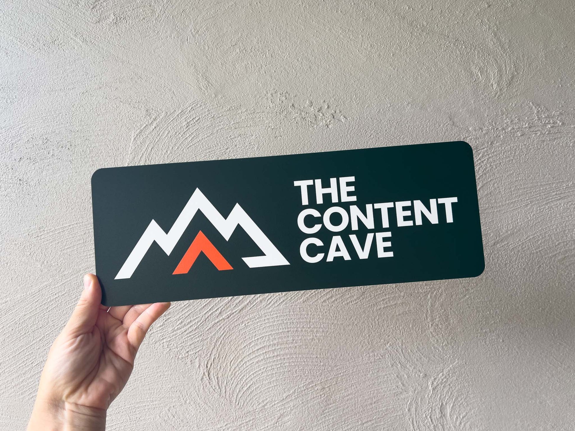 Hand holding a sign with 'The Content Cave' logo against a light gray background