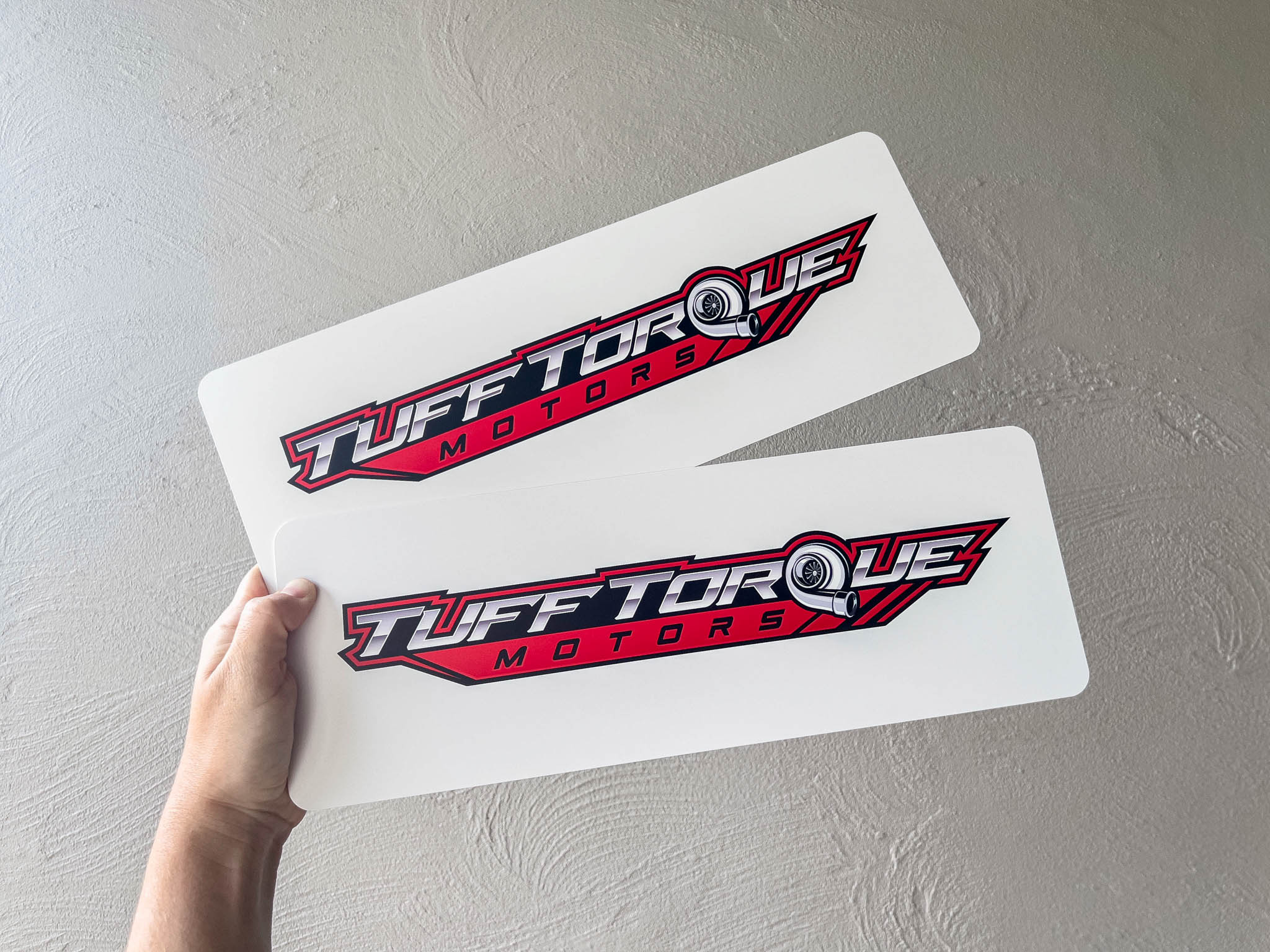 Two 'Tuff Torque Motors' vehicle plates held against a light grey background