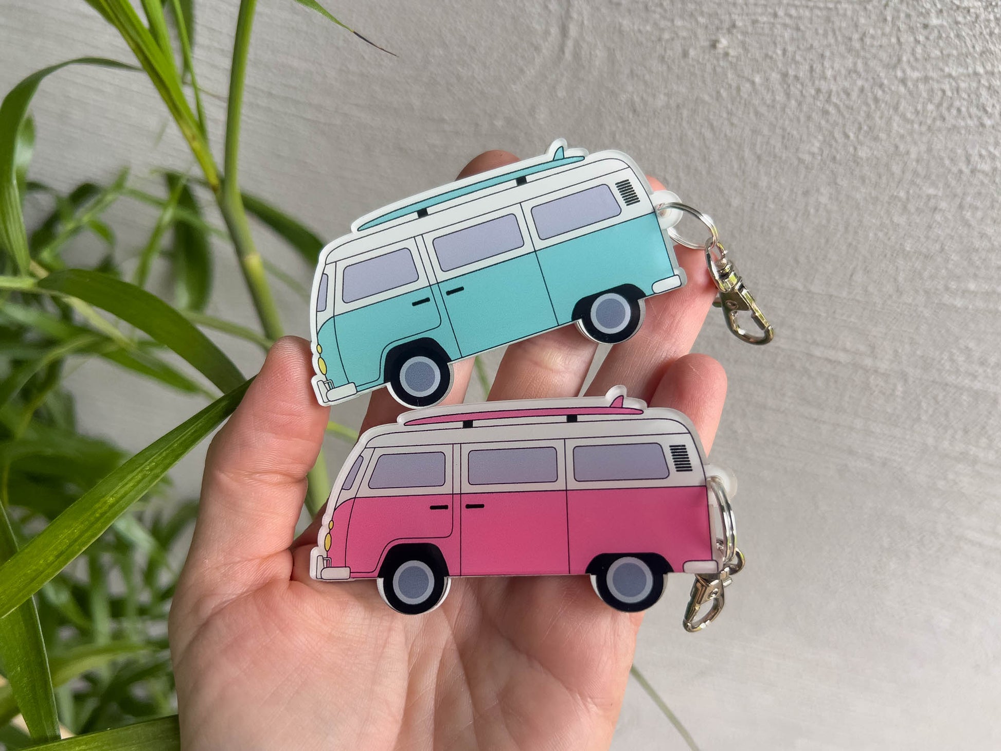 Two custom printed retro-style surf bus keychains held in a hand. One keychain is a light blue mint colour and the other is pink and white.