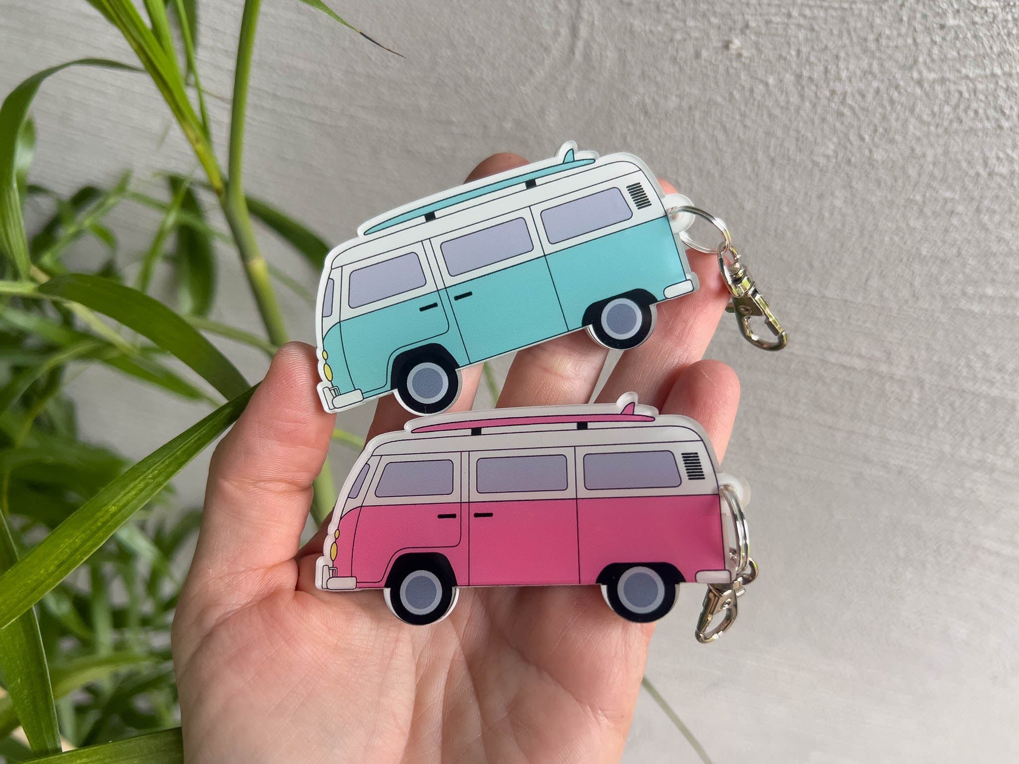 Two custom printed retro-style surf bus keychains held in a hand. One keychain is a light blue mint colour and the other is pink and white.