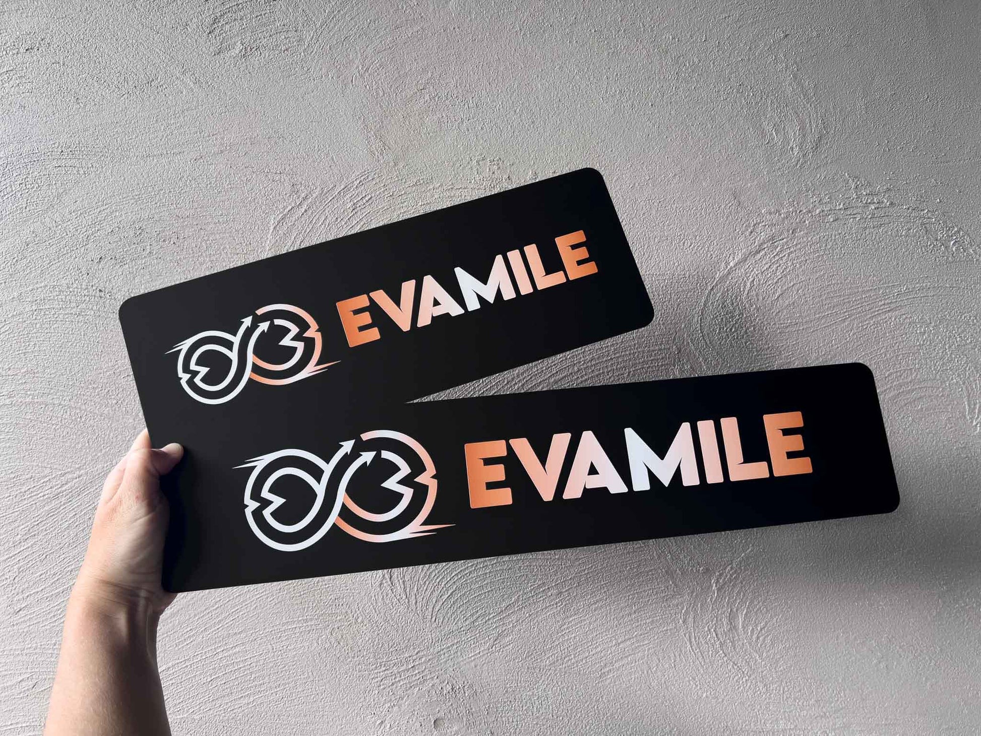 Two custom printed black acrylic logo plates with the brand 'EVAMILE' UV printed with a matte finish.