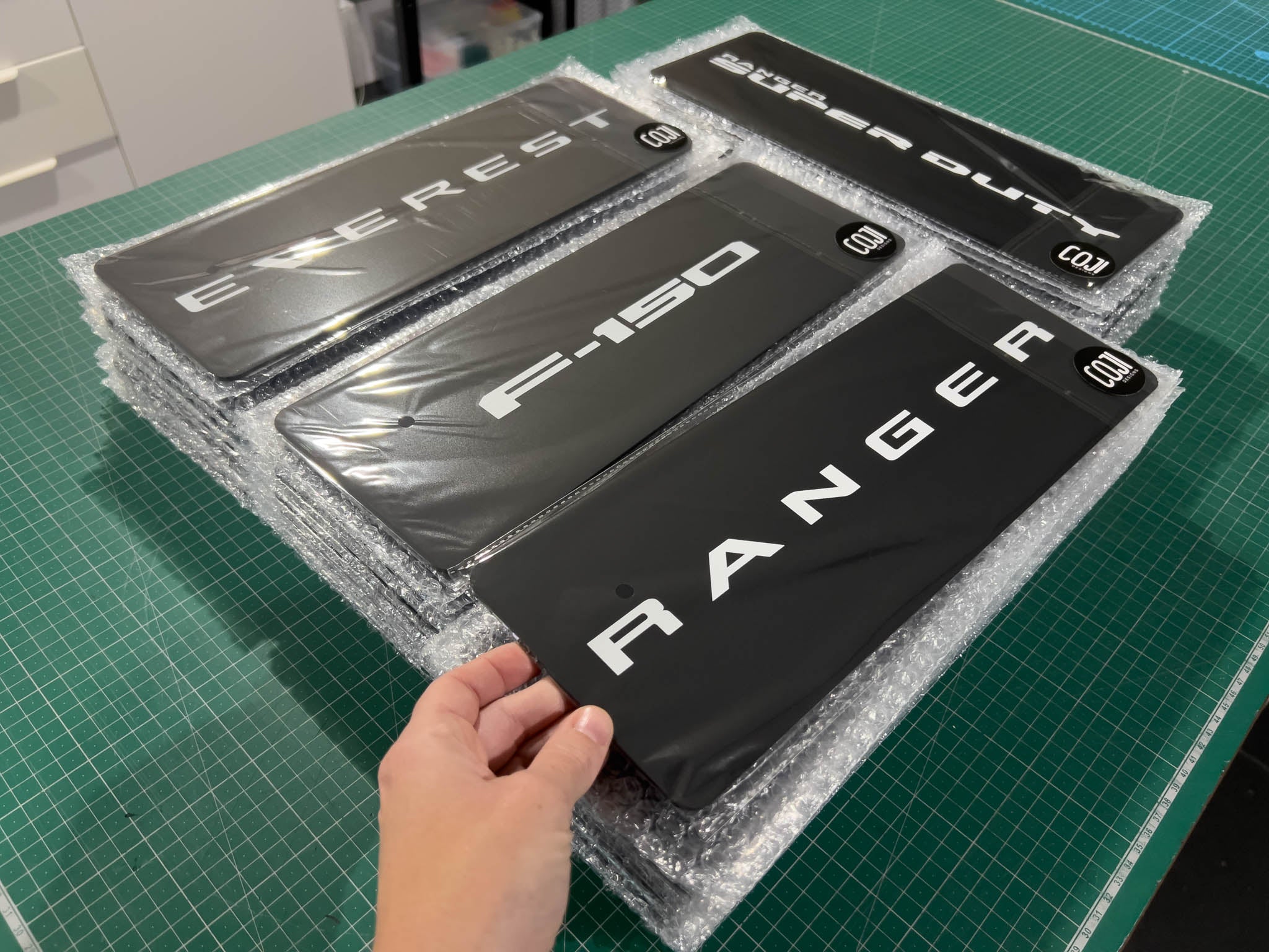 Four black and white acrylic logo plates  for SUVs, including Everest, F-150, and Ranger models for marketing and new model reveals. 