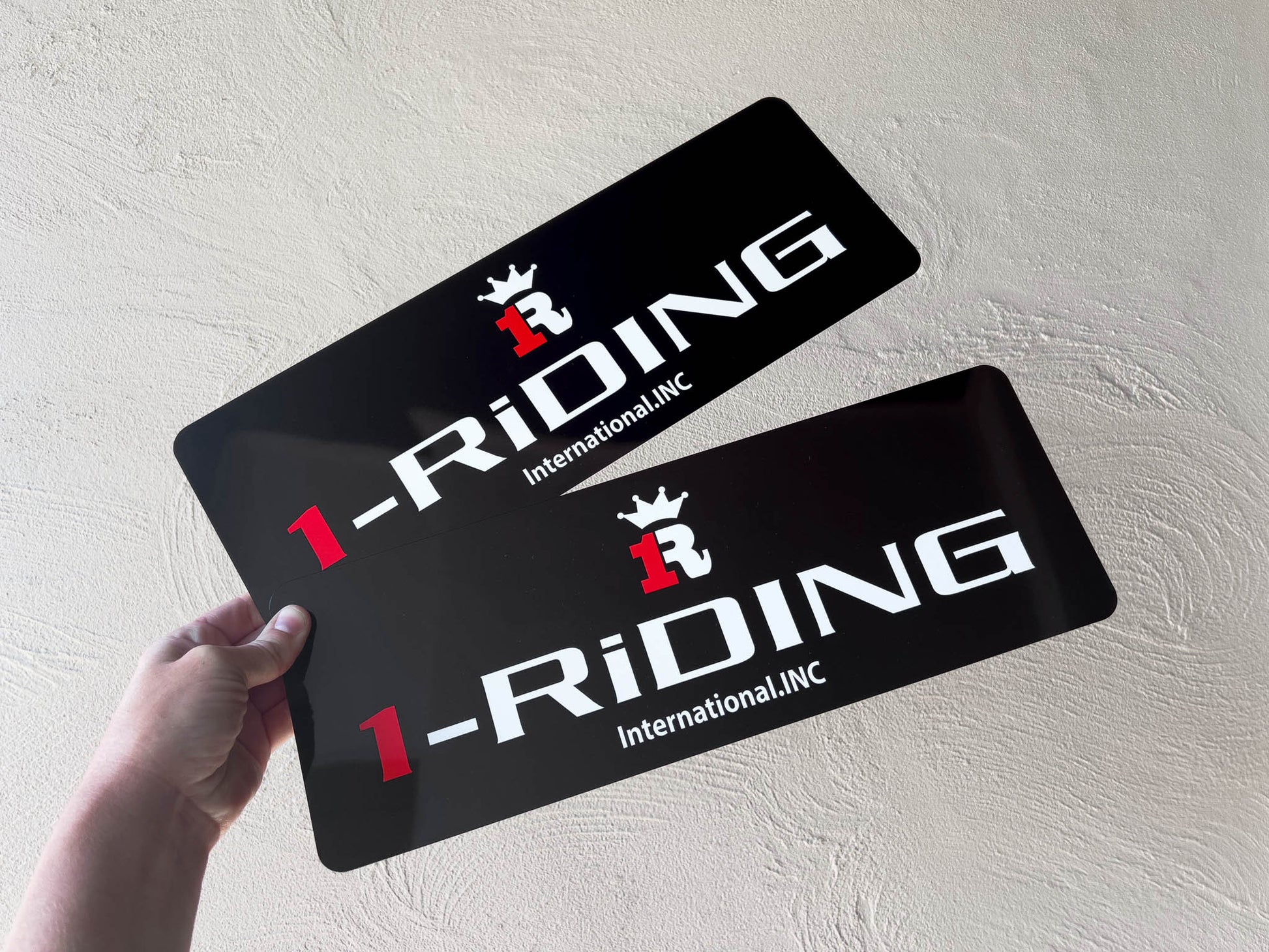 Two black logo plates with '1-Riding International, INC' custom printed onto aluminium plates.