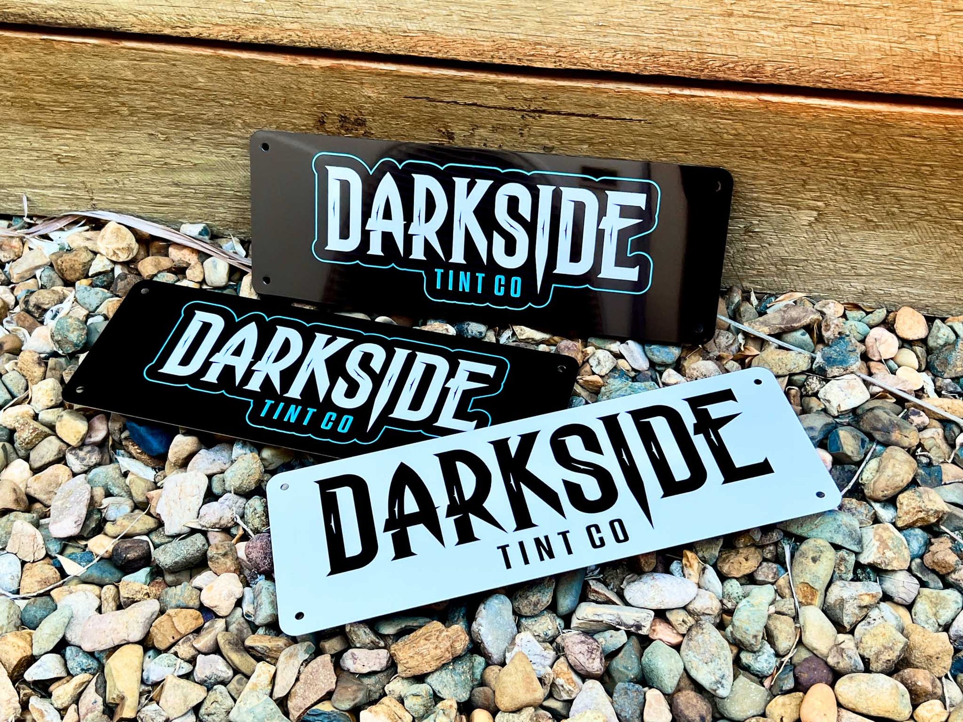 Three 'Darkside Tint Co' signs on a gravel surface
