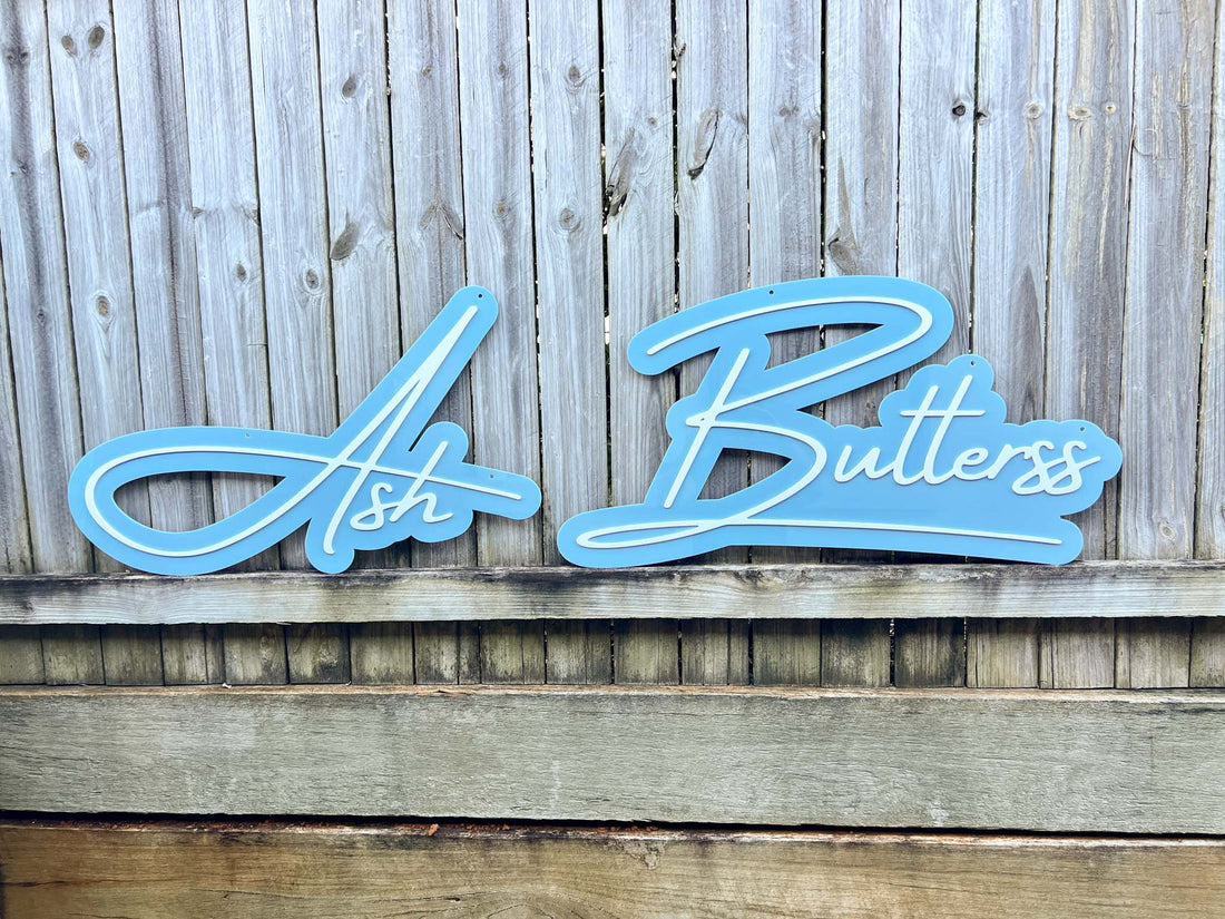 A blue and white custom shape acrylic sign that reads 'Ash Butterss'.