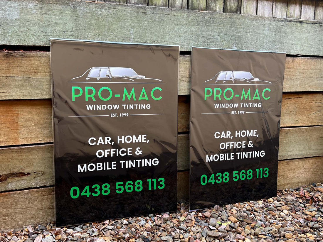 Two custom printed Pro-Mac Window Tinting signs against a wooden background.