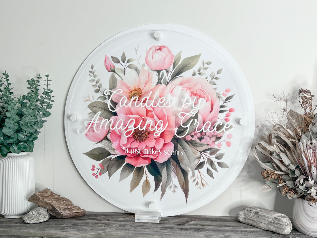 Decorative round business logo sign with a floral design and text 'Candles by Amazing Grace' on a white wall.