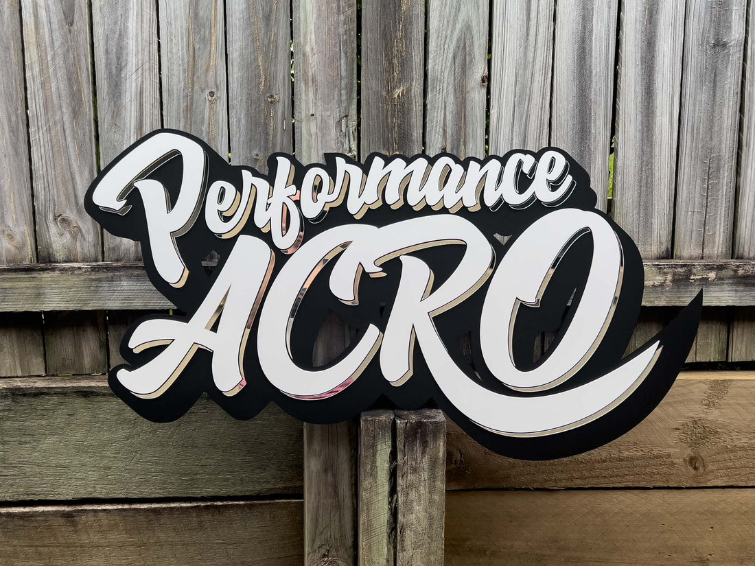 Custom shape acrylic business sign for Performance Acro sitting on a wooden fence.