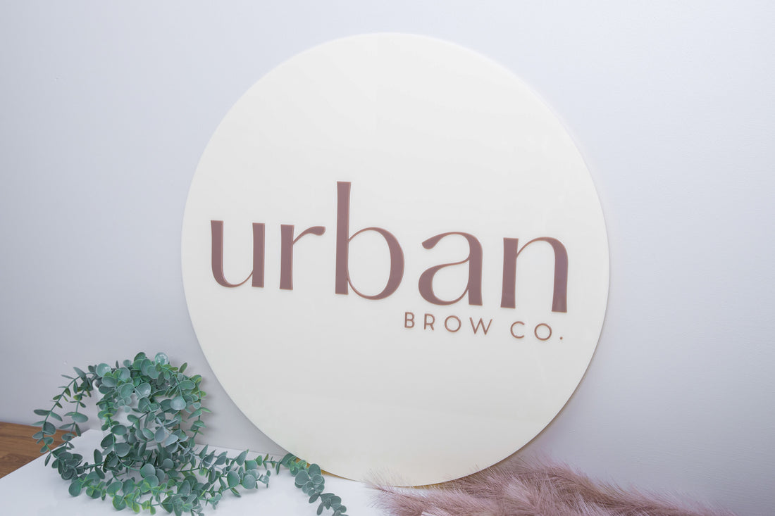 Round beige acrylic logo sign with 'urban brow co.'