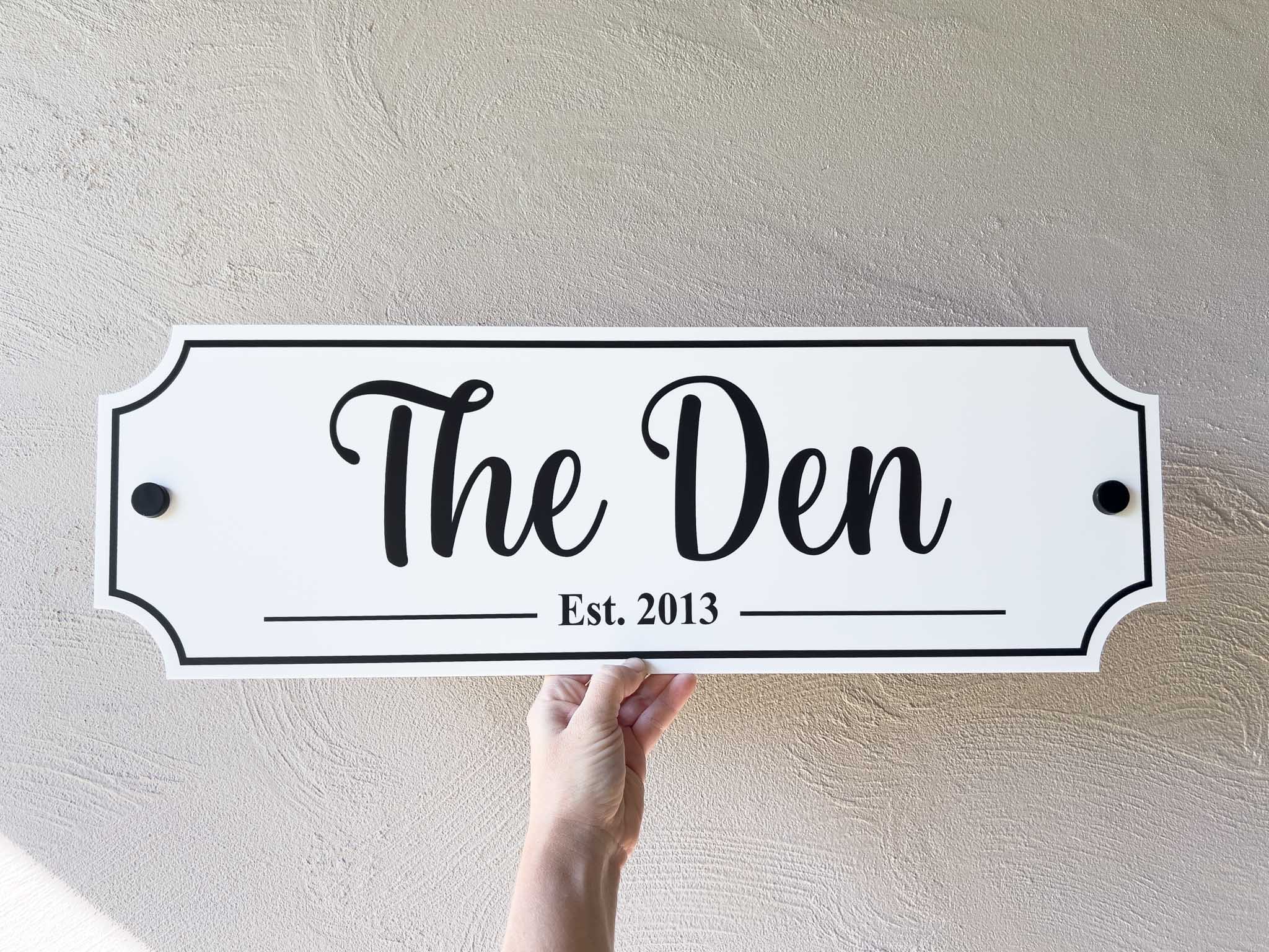 A white and black classic Maison sign with the text 'The Den Est. 2013'.