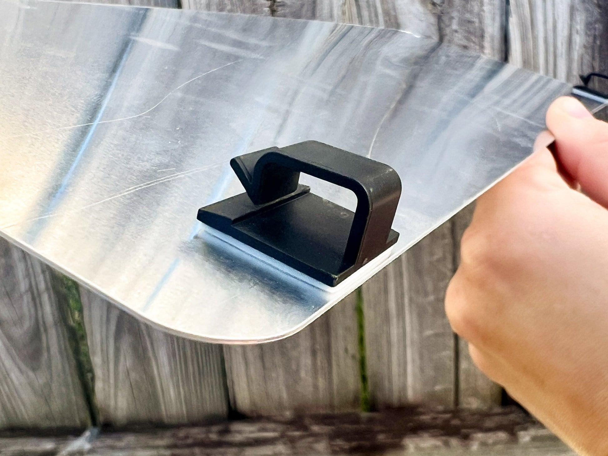 Hand holding an aluminium logo plate with two black plastic mounting clips.