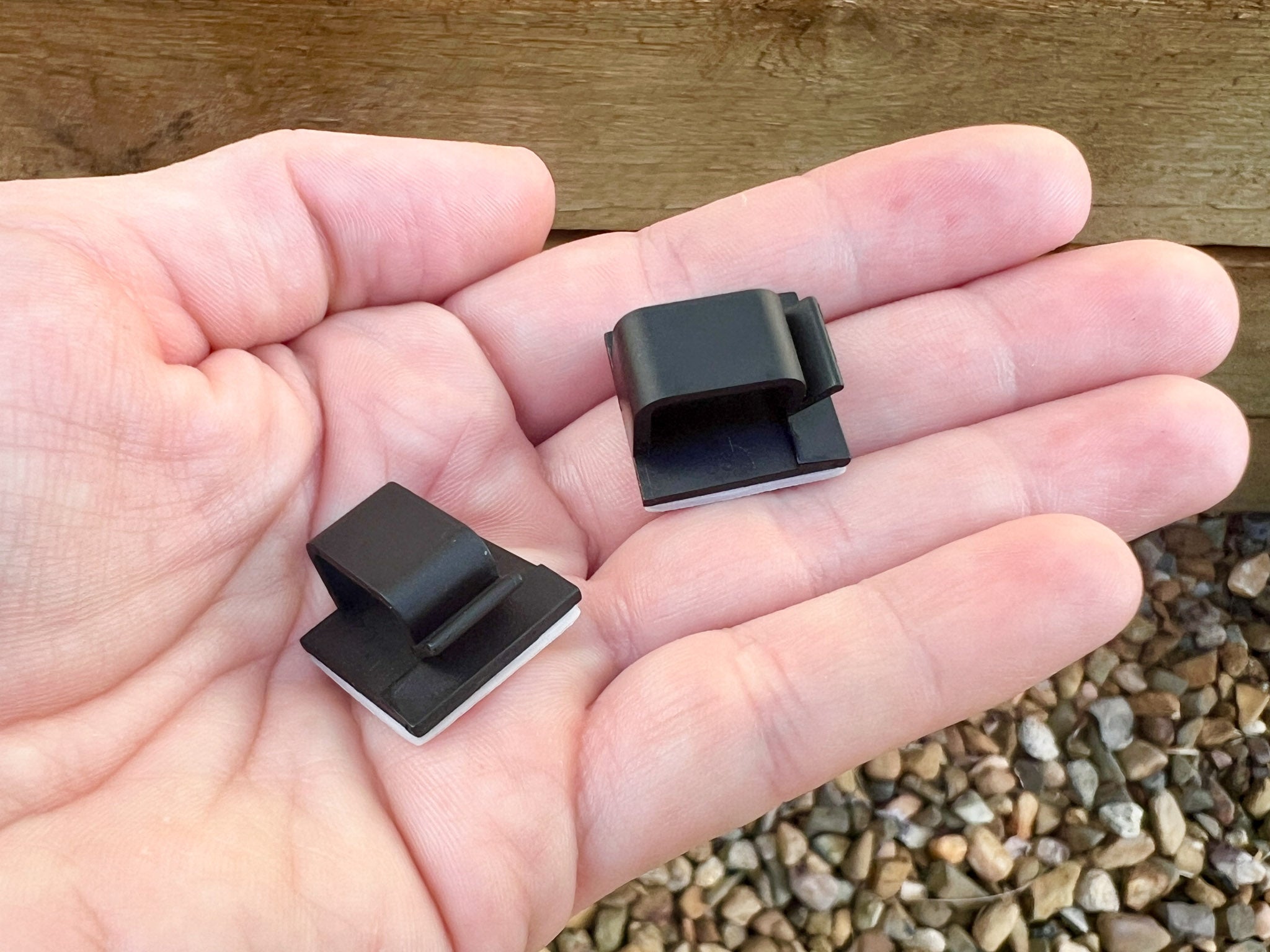 Two black logo plate clips being displayed on a hand for size comparison