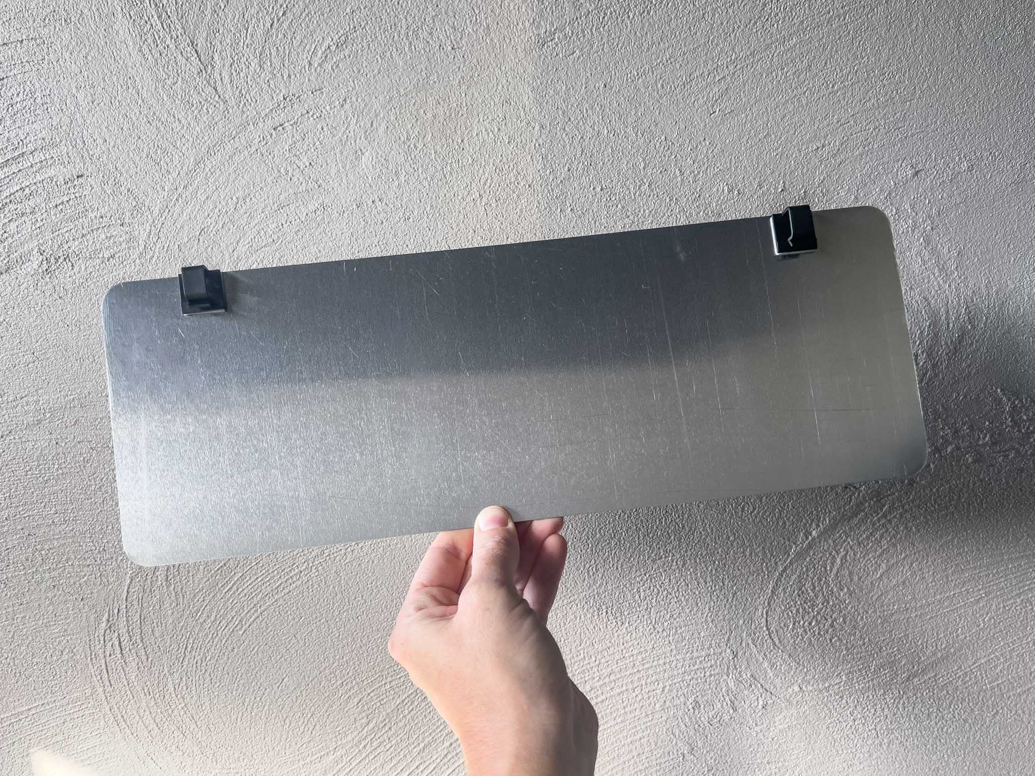 Hand holding an aluminium plate with mounting clips attached to the back.