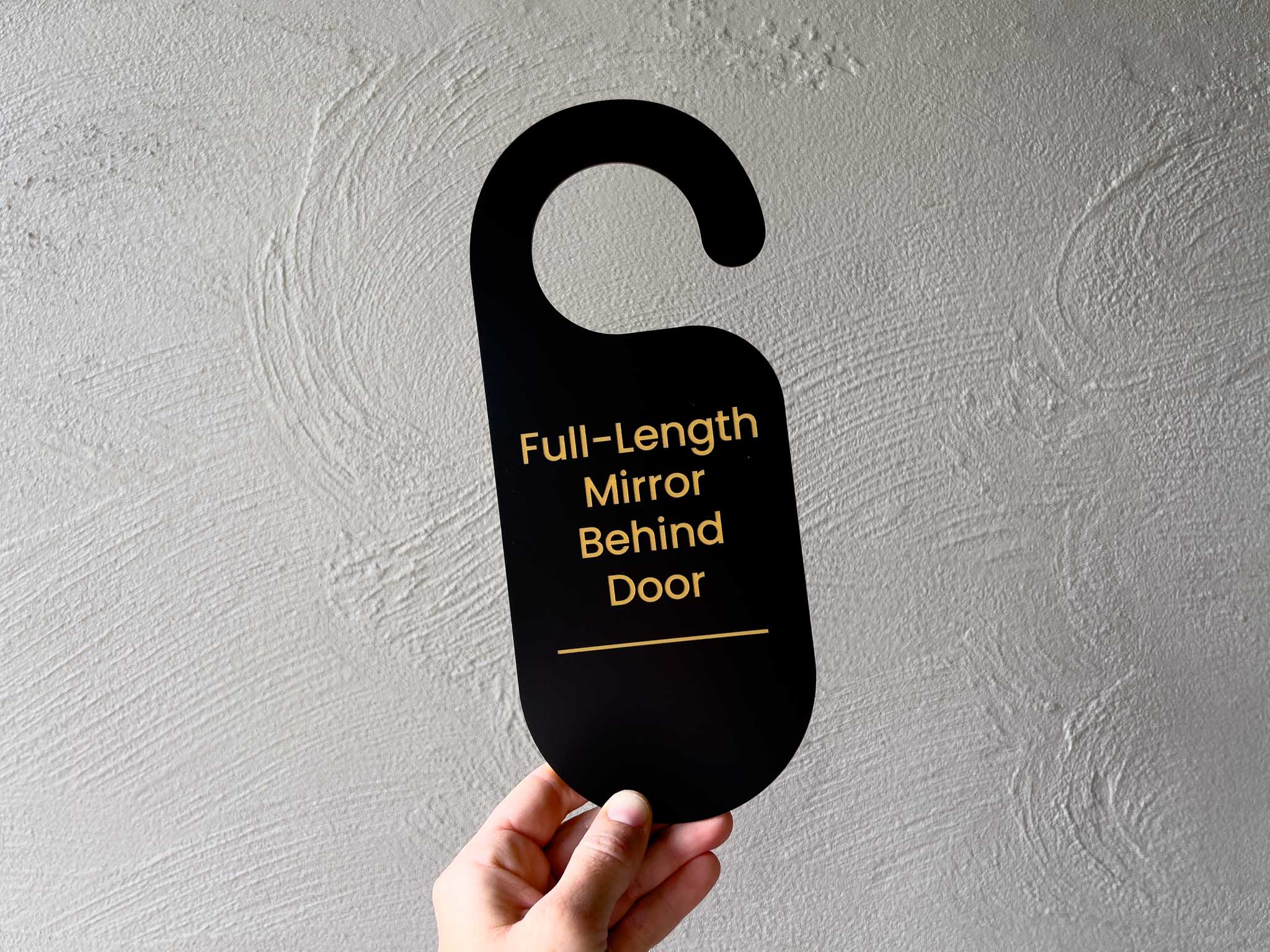 A personalised black and gold engraved flexi door hanger that says 'Full-Length Mirror Behind Door' for dressing room.