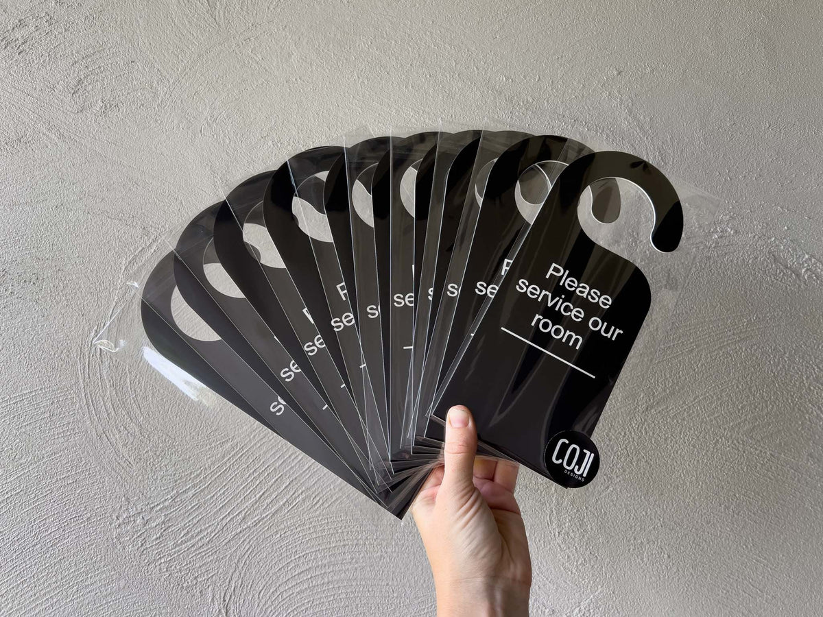 A collection of black and white custom engraved door hangers that read 'Please service our room'.