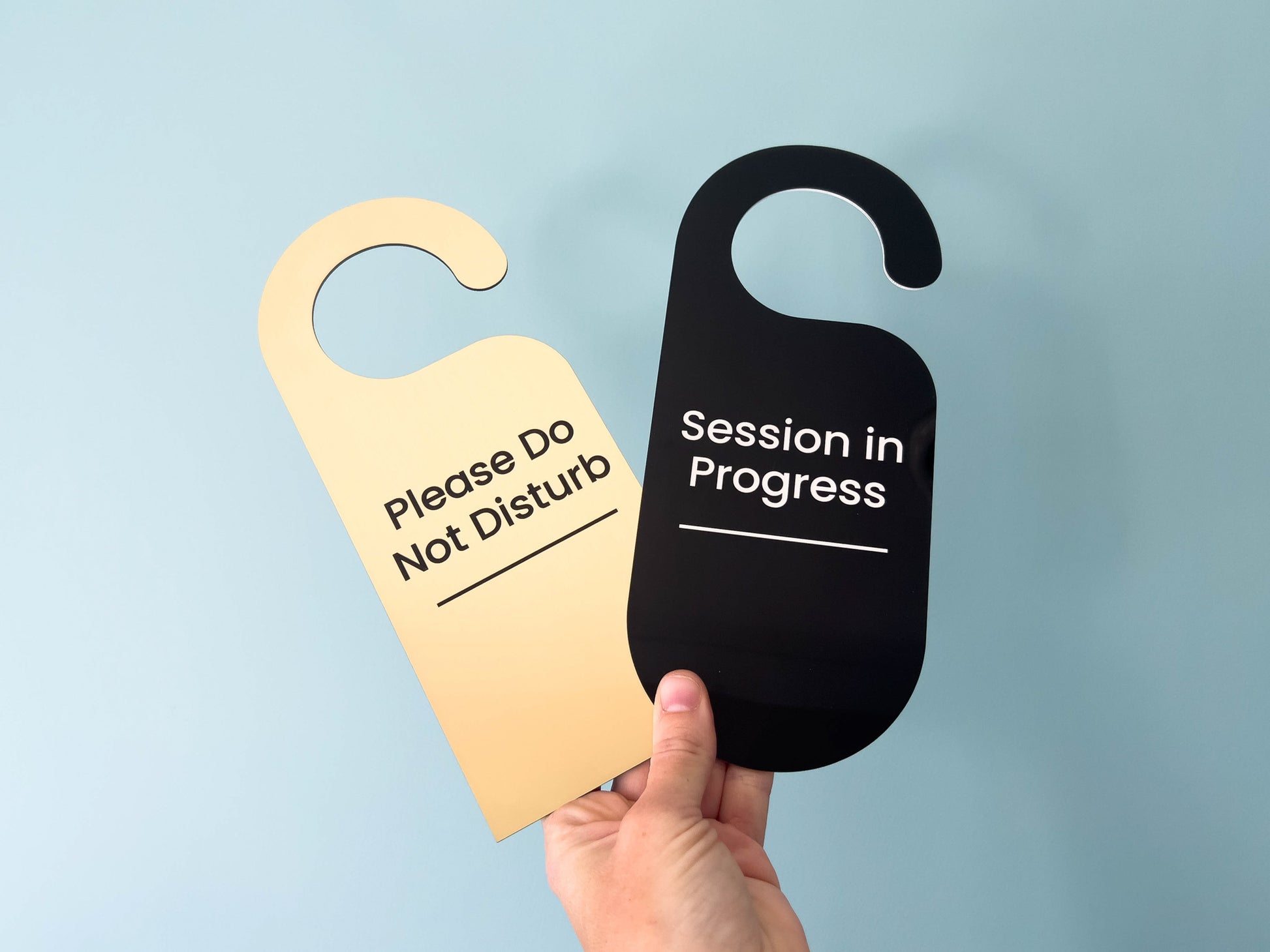 Two custom door hangers in black and brushed gold with custom engraved text.