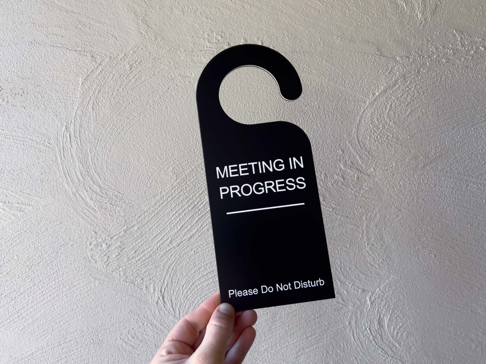 Hand holding a custom black and white door hanger used to hang on the door handle when meetings are in progress.