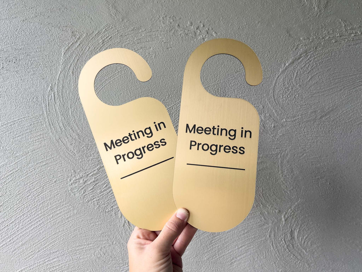 Two round personalised brushed gold engraved door hangers that read 'Meeting in Progress',