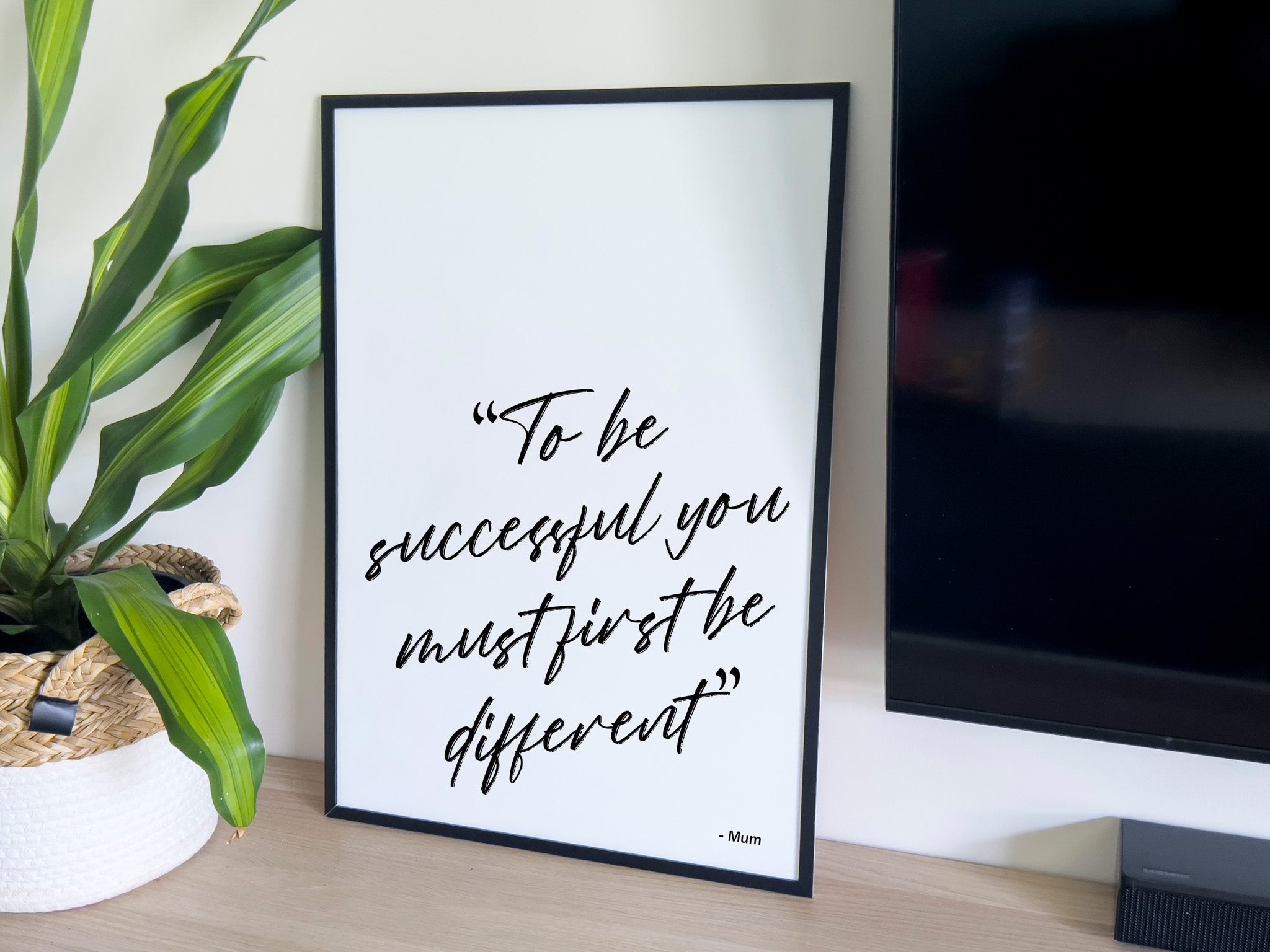 Framed motivational quote on a desk with a plant and computer monitor in the background