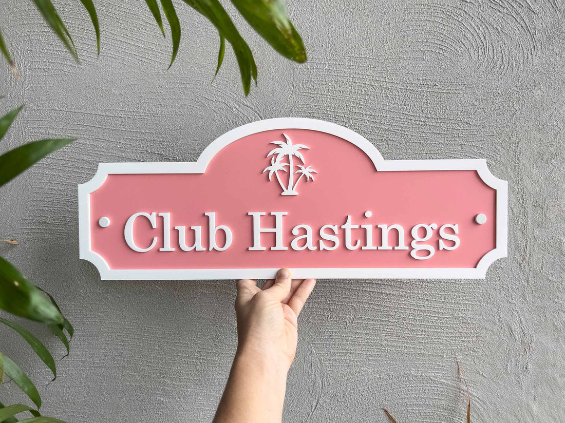 A tropical melon and white palm tree sign with 'Club Hastings'.