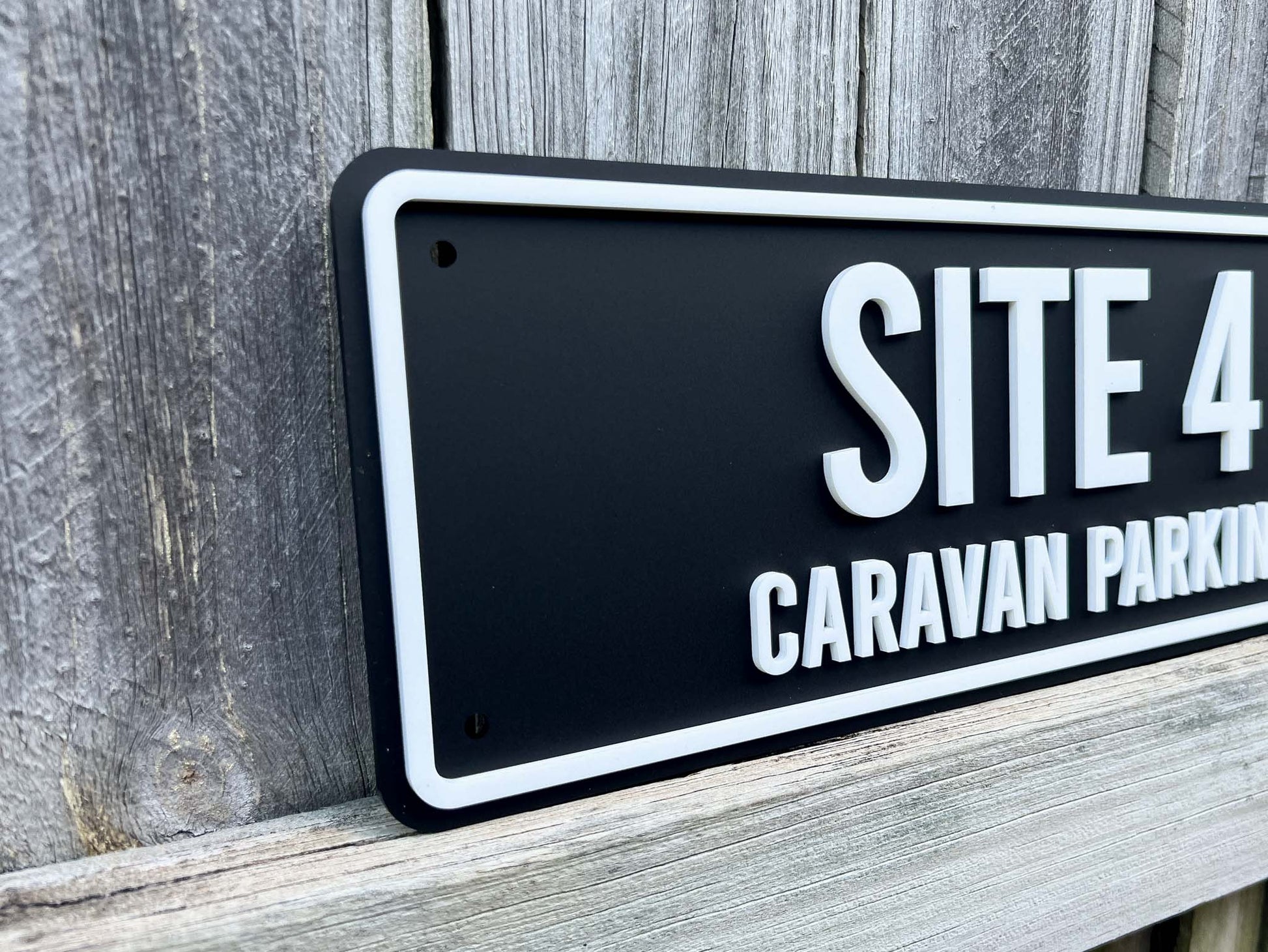 Black sign with white text 'SITE 4 CARAVAN PARKING' on a wooden background