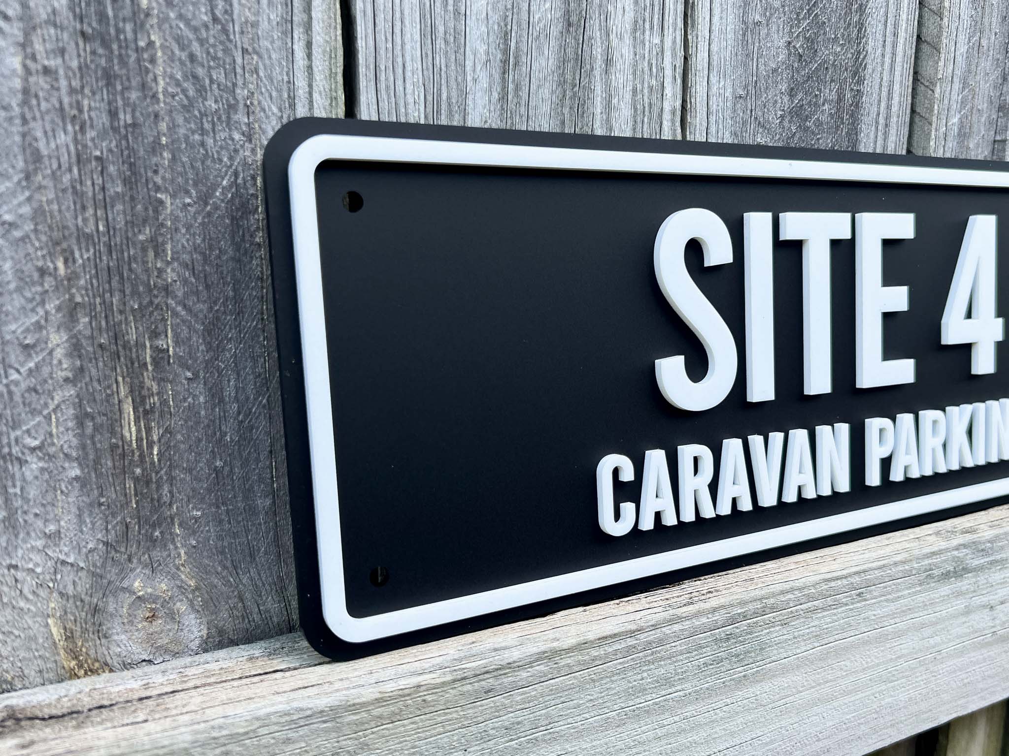 Black sign with white text 'SITE 4 CARAVAN PARKING' on a wooden background