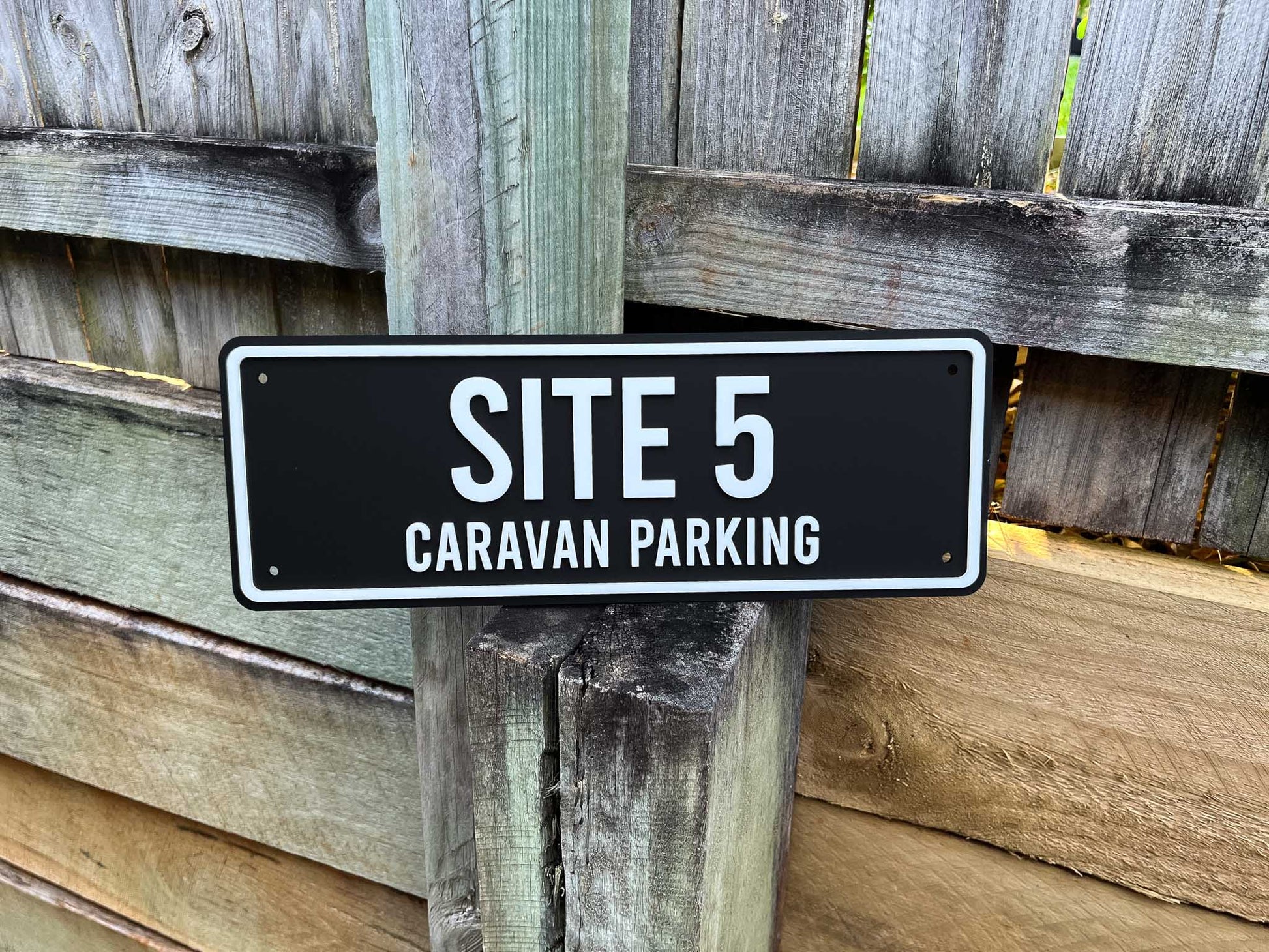 Acrylic black and white sign reading 'SITE 5 CARAVAN PARKING' sitting on a wooden pole.