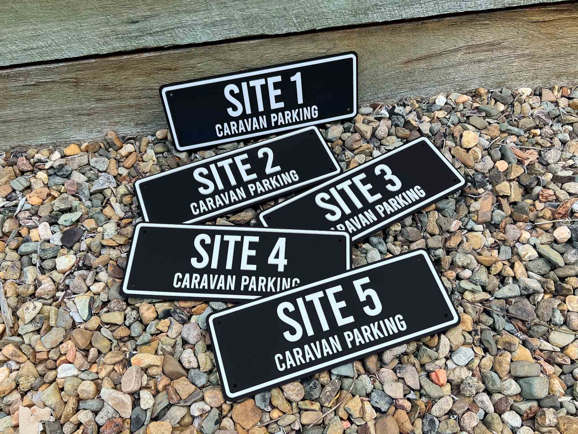 Five black and white caravan parking signs labeled Site 1 to Site 5 on a gravel surface.