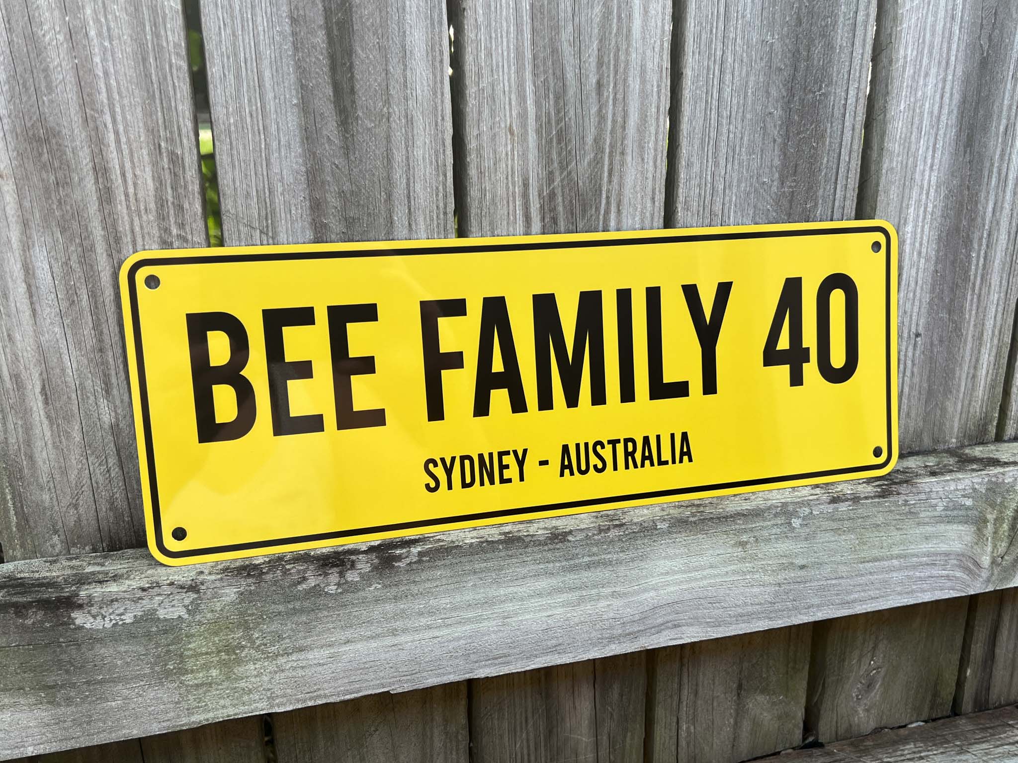 Yellow and black custom printed sign with 'BEE FAMILY 40' text on a wooden background