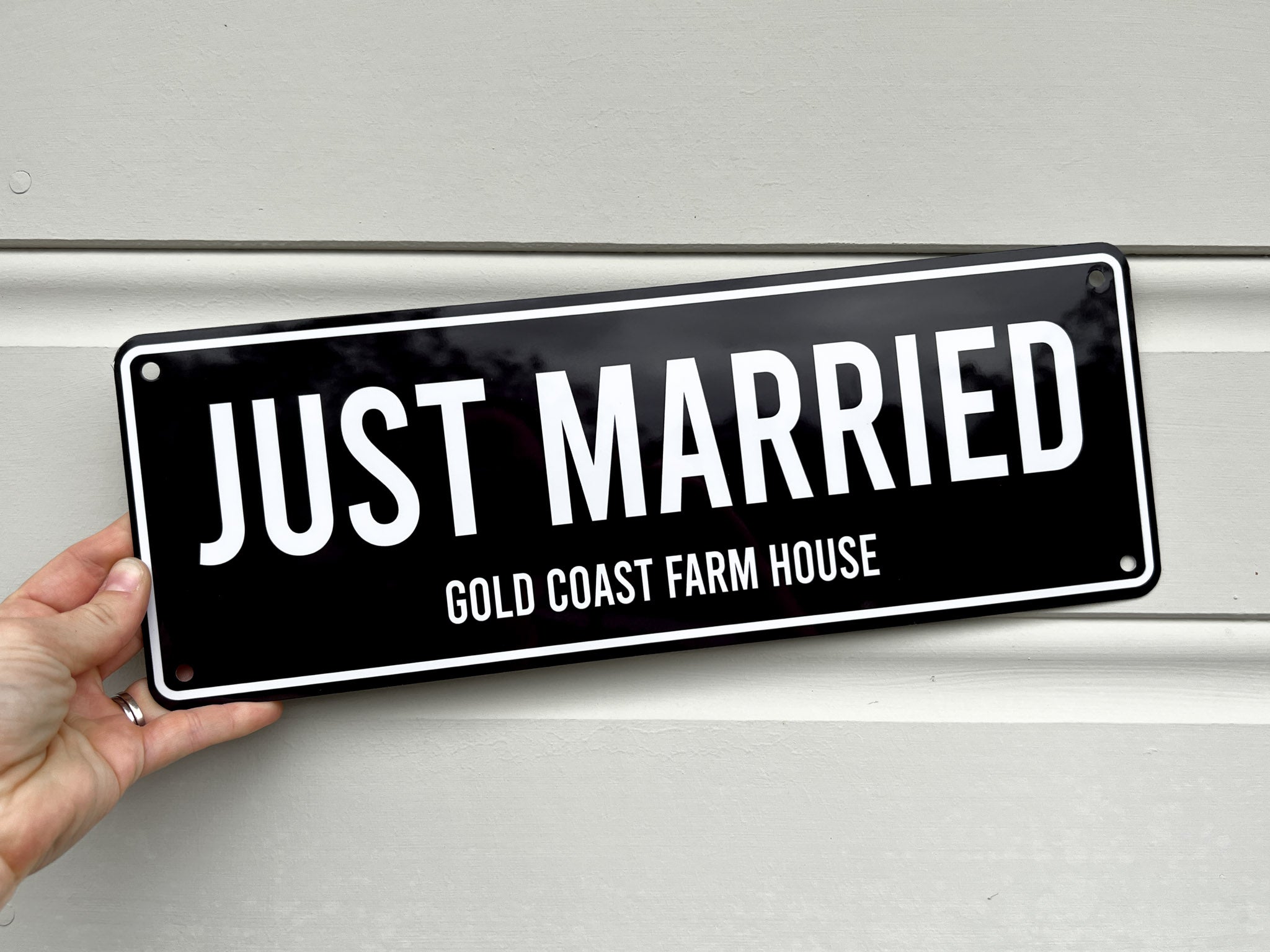 Hand holding a 'Just Married' sign with text on a plain background