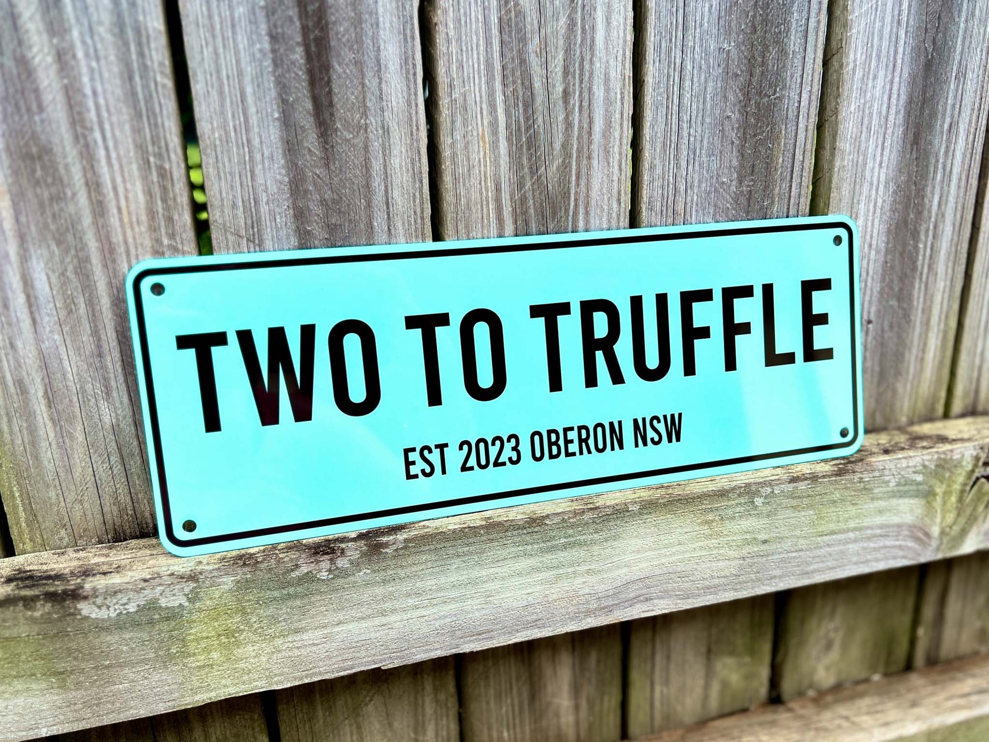 Mint green teal sign with 'TWO TO TRUFFLE' text on a wooden background