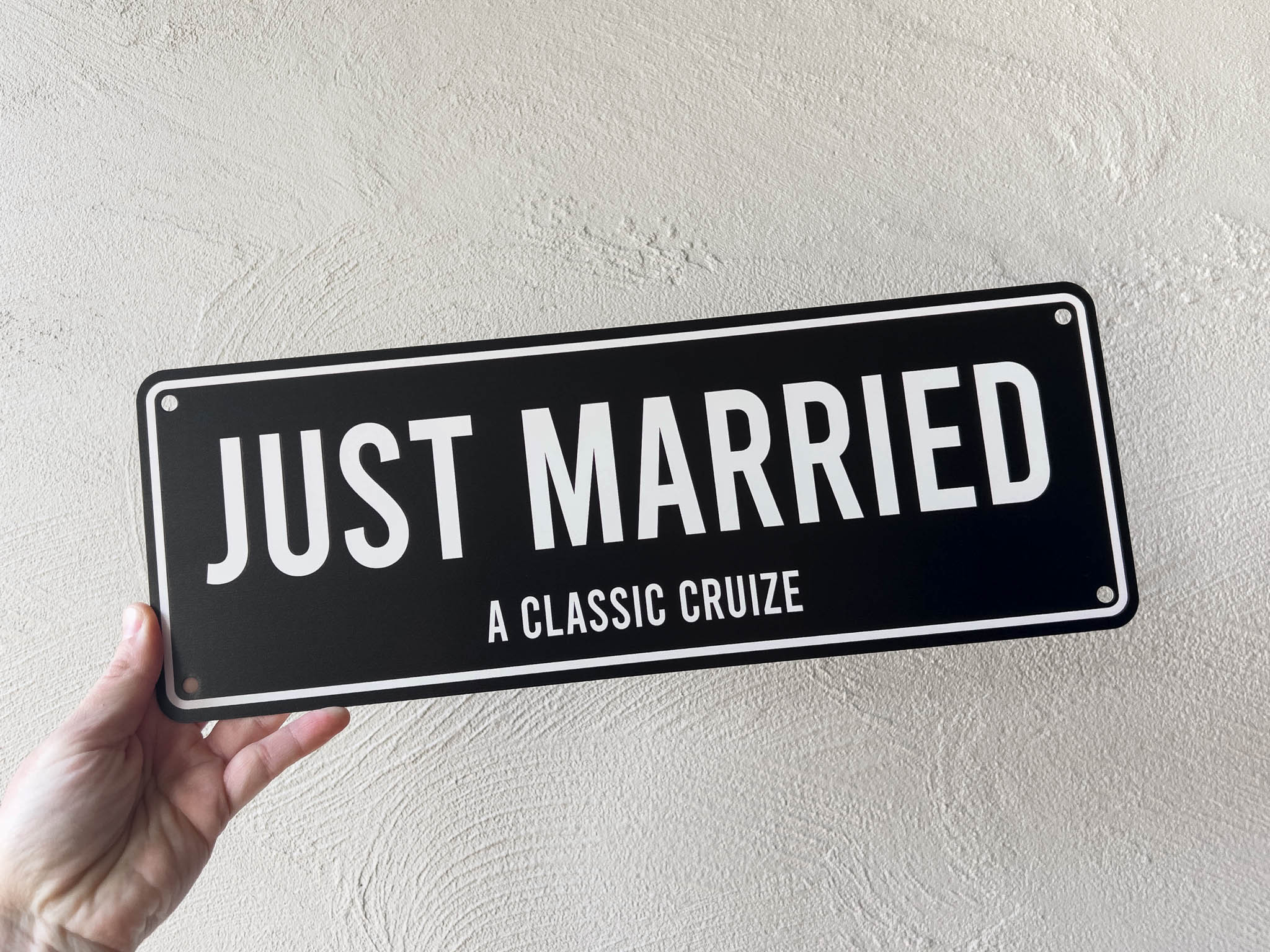 Hand holding a 'Just Married' sign against a light grey background