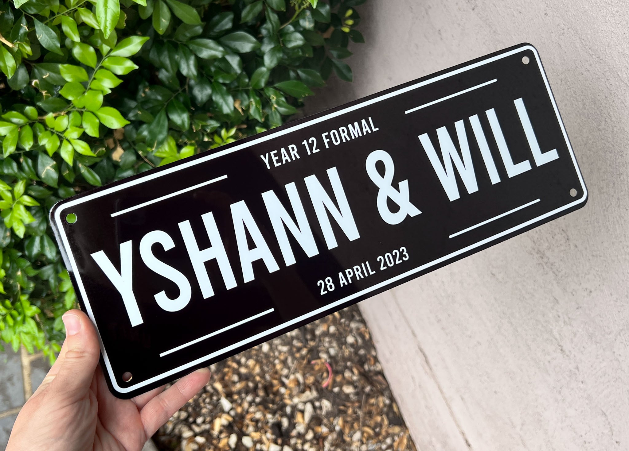 Personalised sign with names 'Yshann & Will' and Year 12 Formal event details, held against a natural background.