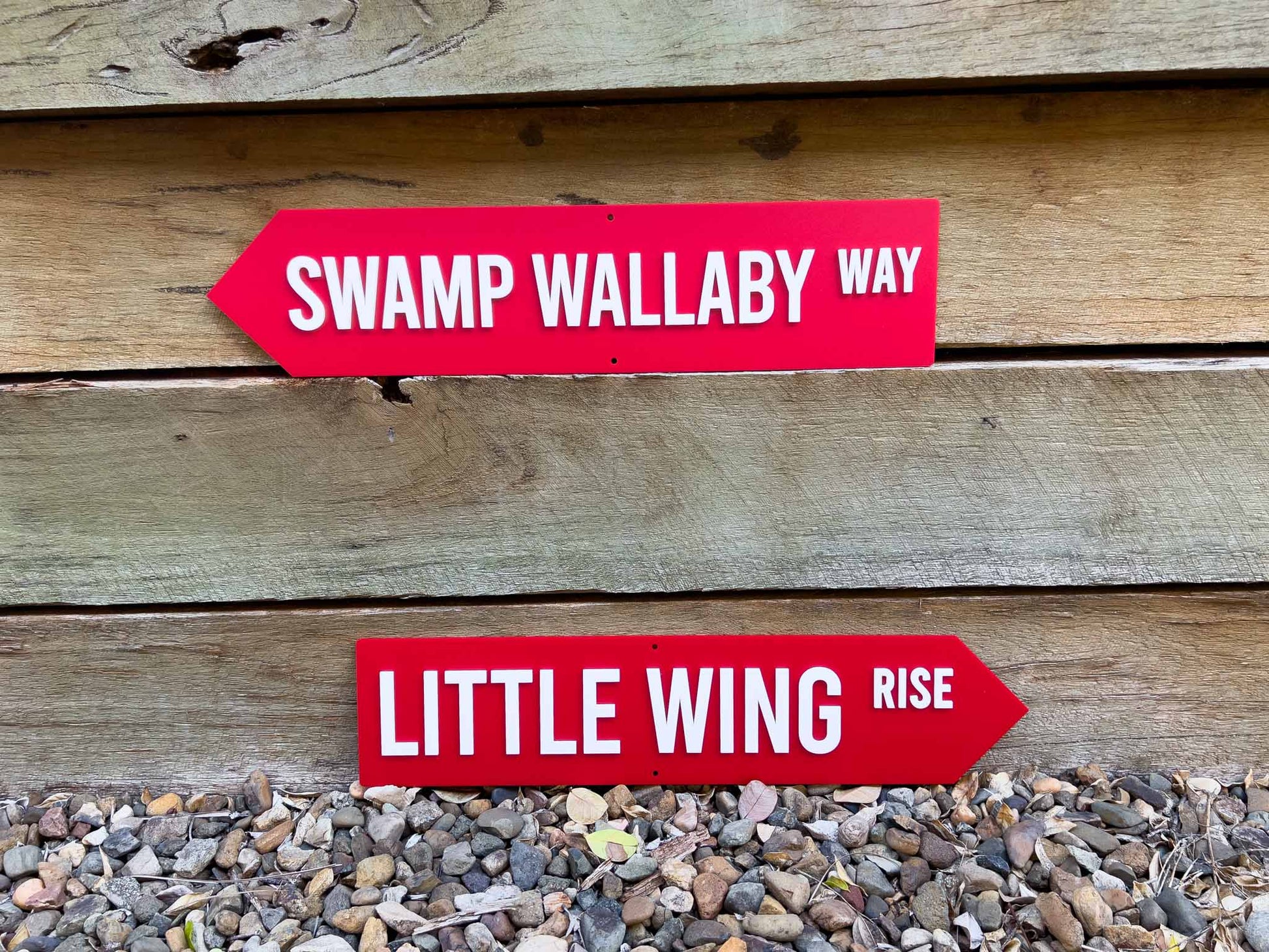 Two red and white street style signs that say 'SWAMP WALLABY WAY' & 'LITTLE WING RISE'.